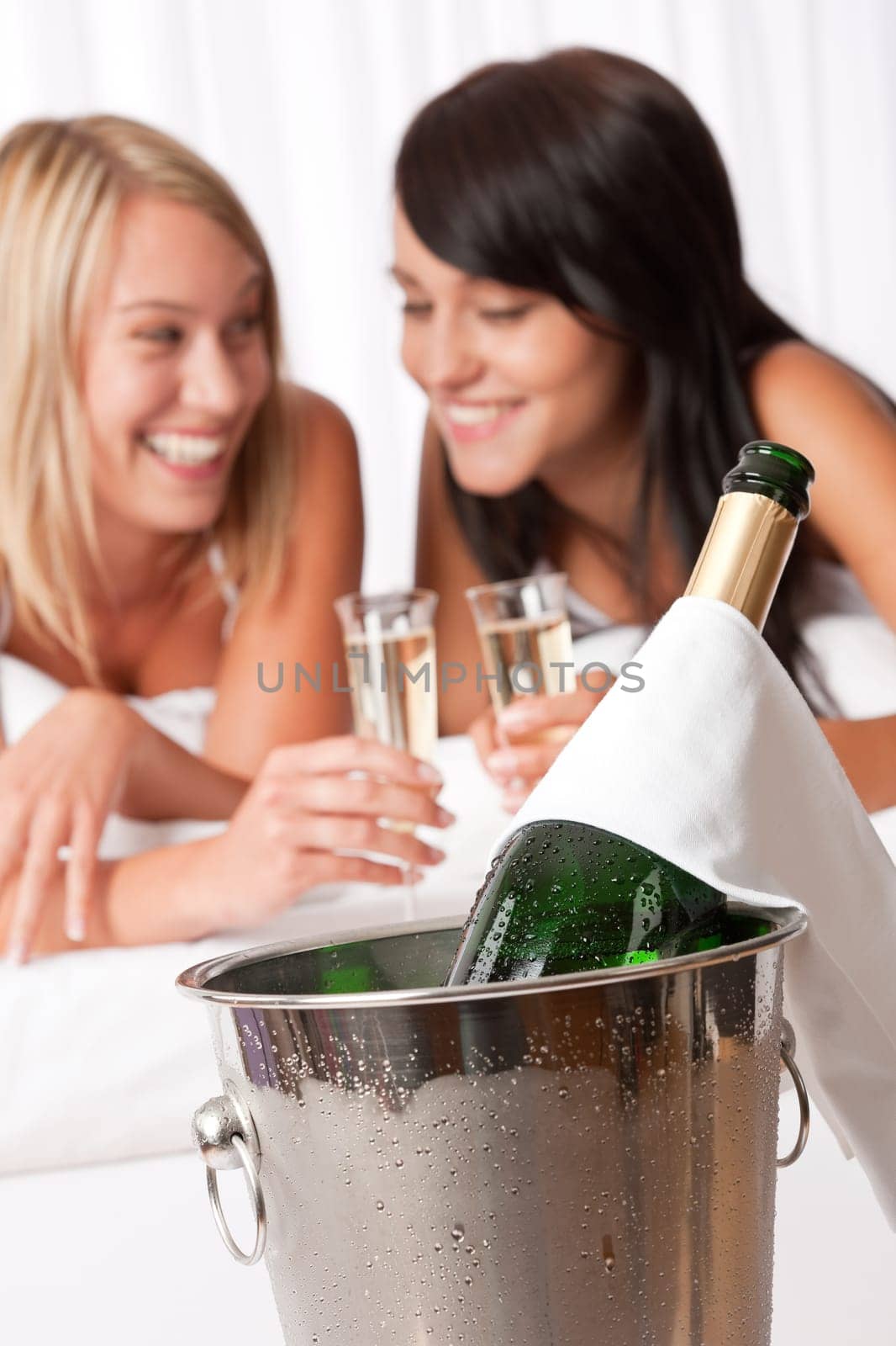 Two women toasting with champagne in bedroom