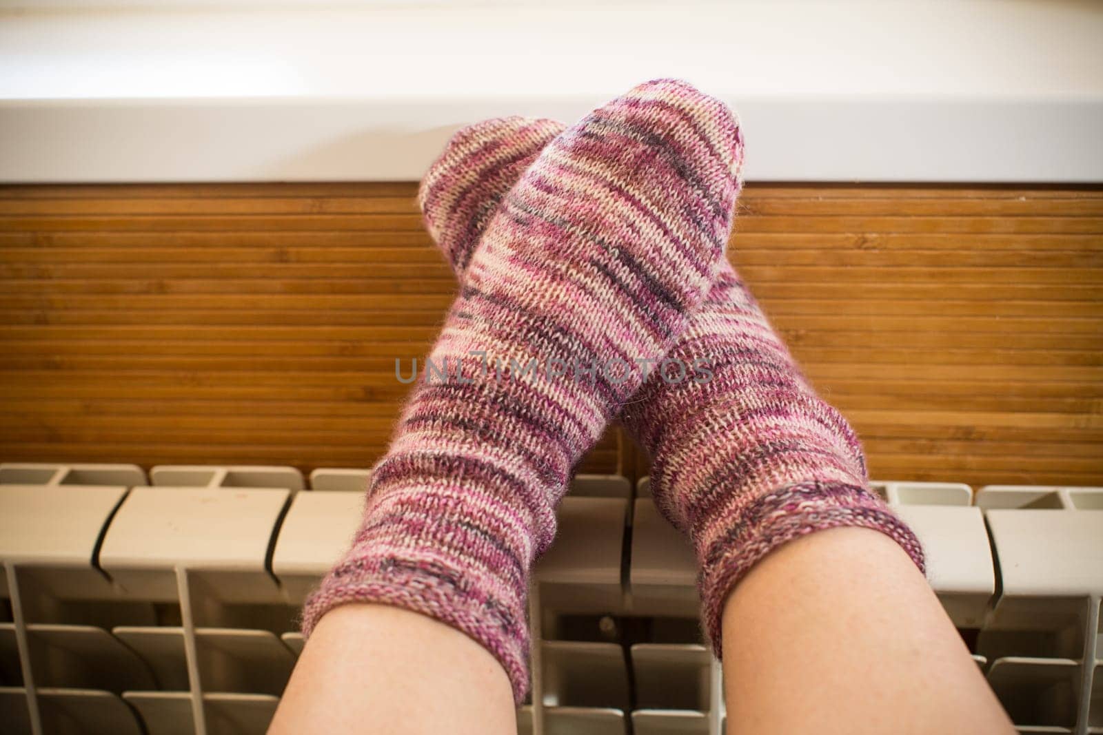 Feet in warm winter socks warm up on the radiator. by Rawlik
