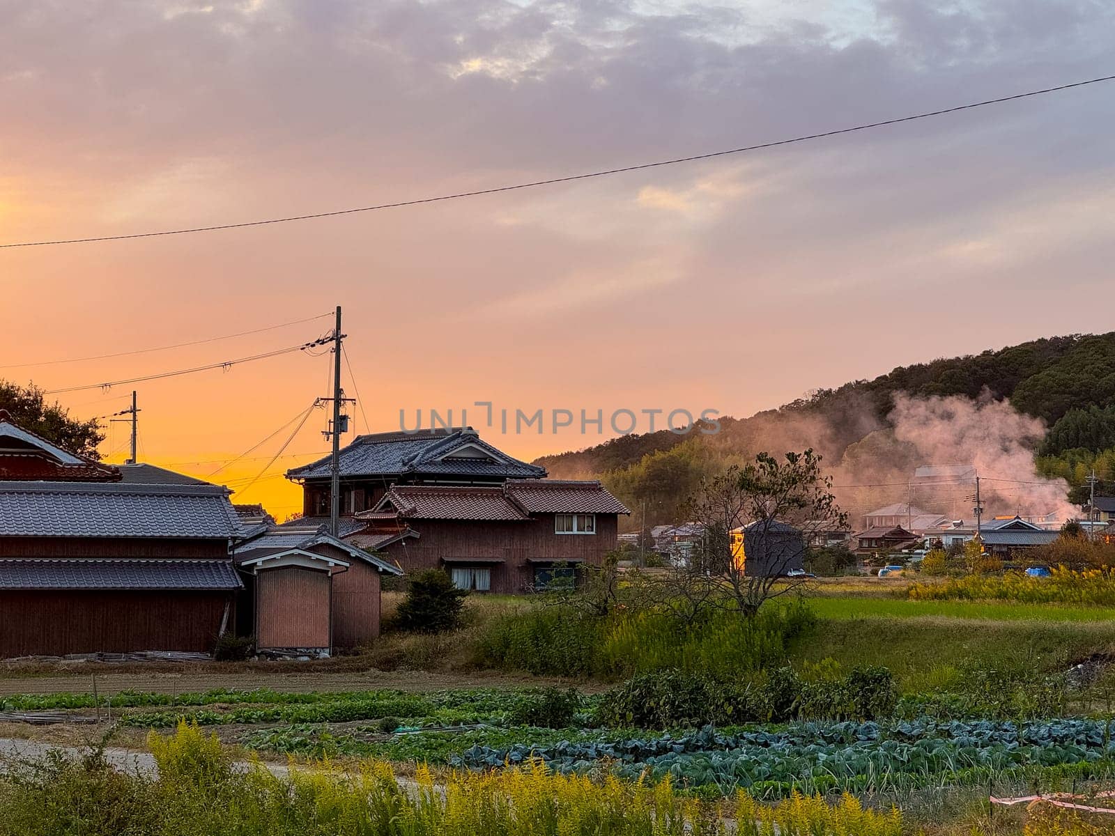 Smoke rises from fire by traditional houses in rural Japan with sunset glow in sky. High quality photo