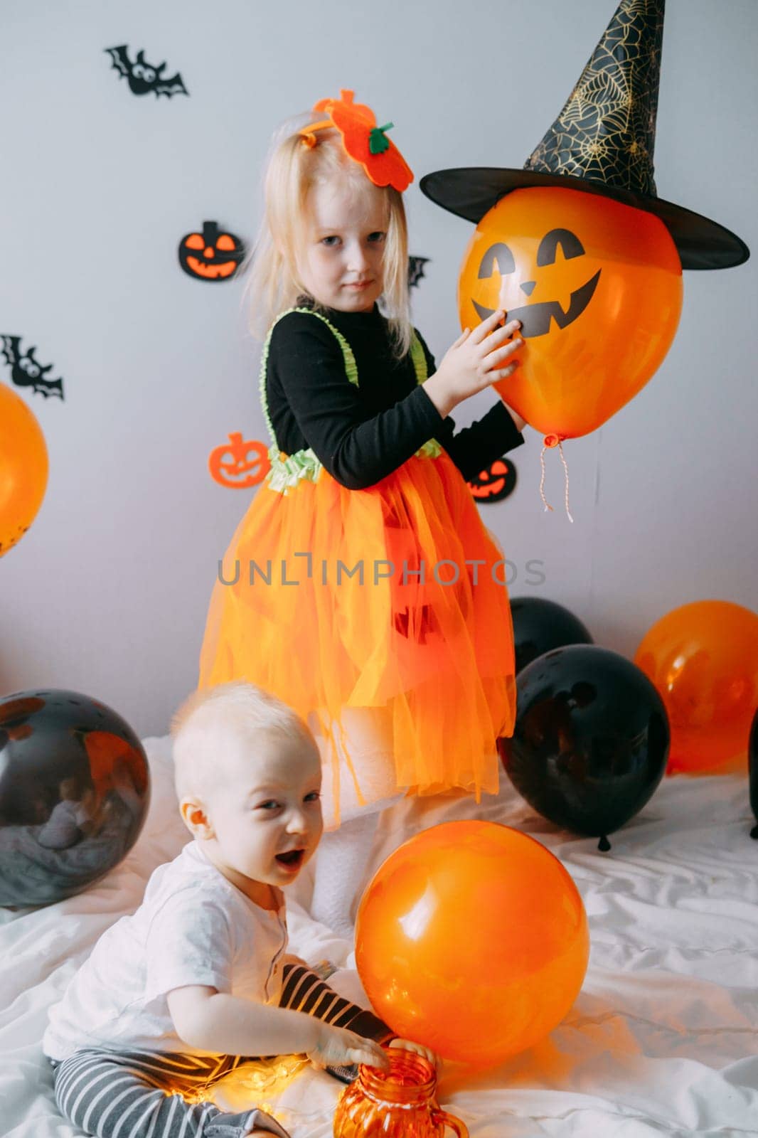 Children's Halloween - a girl in a witch hat and a carnival costume with airy orange and black balloons at home. Ready to celebrate Halloween.