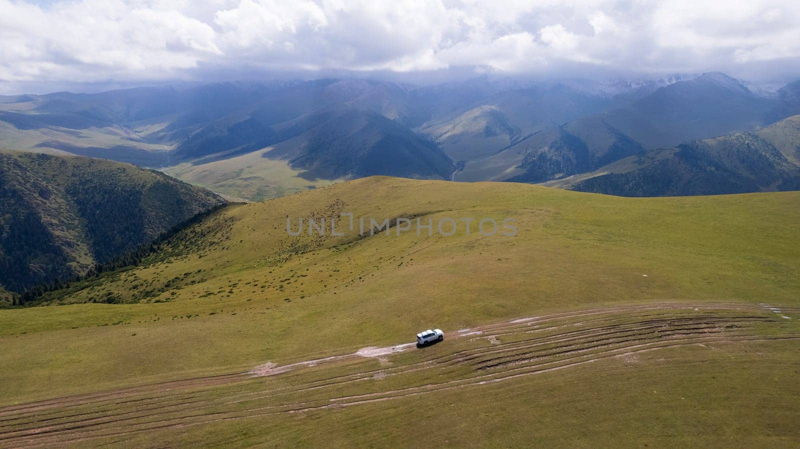 A white SUV rides in the mountains through fields by Passcal