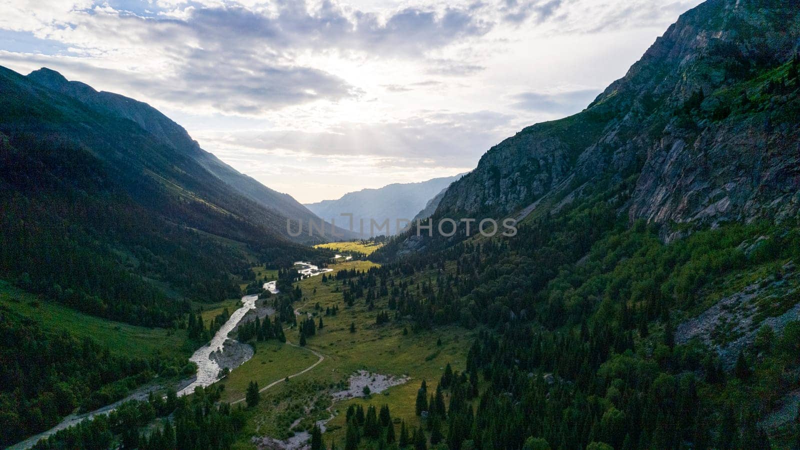 Beautiful sunset with a view of the green gorge and the river. coniferous trees, forests, lots of grass are all around. A seething gray river. Clouds in the sky. The rays of the sun. Steep cliffs