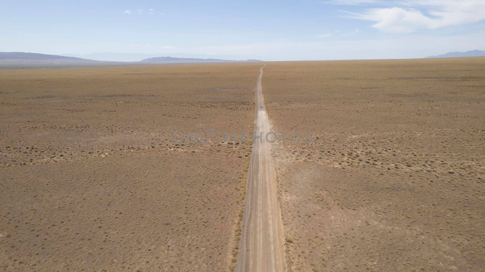 A white SUV is driving fast on a dusty road. Drone by Passcal