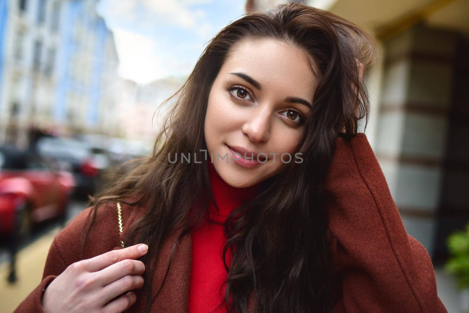 portrait of a fashionably dressed woman posing for the camera in a brown coat and red sweater by Nickstock
