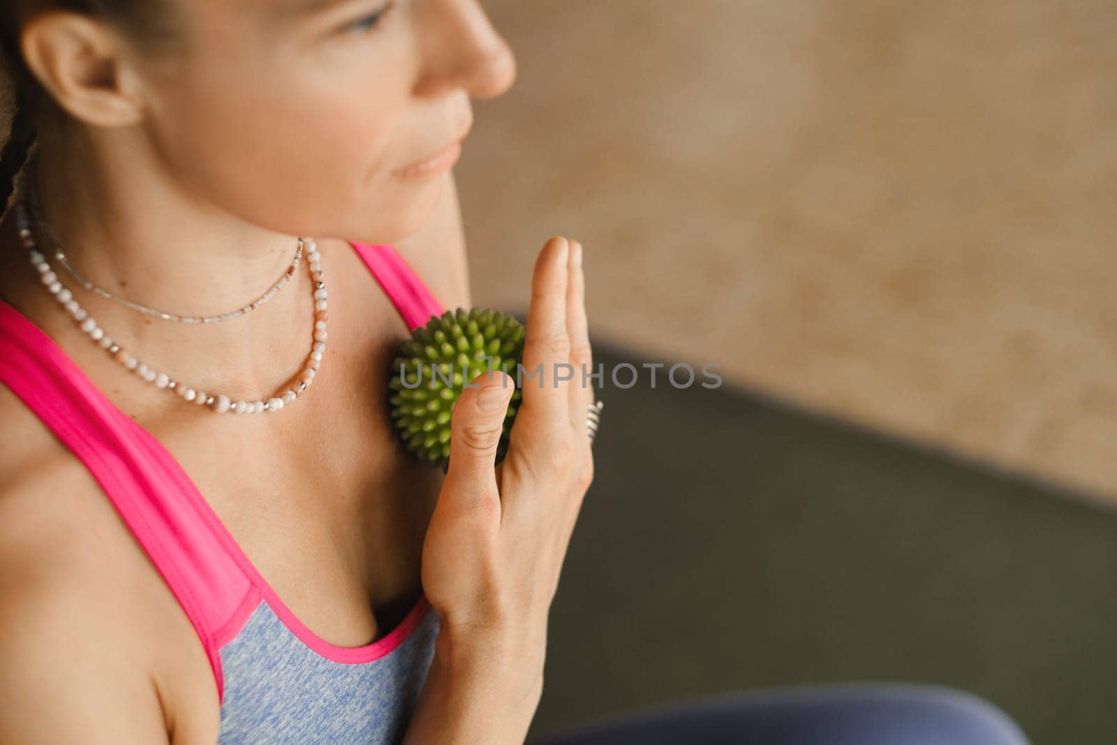 A woman does self - massage with a small ball while sitting in a fitness room . Myofascial relaxation.