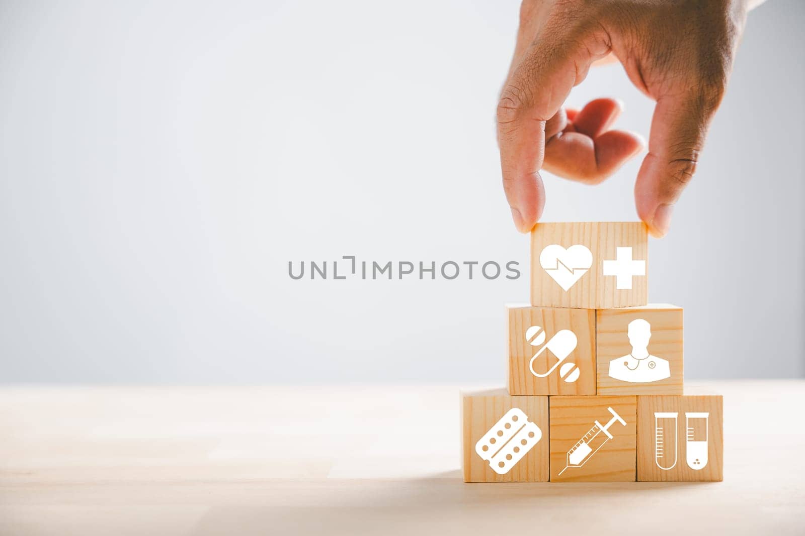 Hand holds wooden block featuring healthcare and medical icons, portraying safety, health, and family well-being. Evoking pharmacy, heart care, and happiness. health care concept