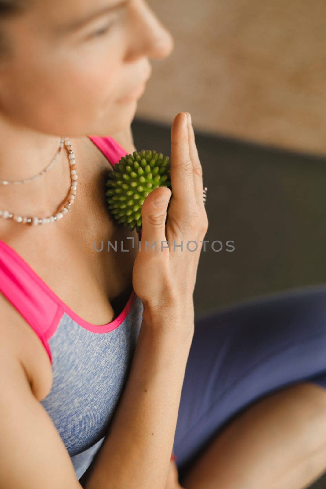A woman does self - massage with a small ball while sitting in a fitness room . Myofascial relaxation by Lobachad