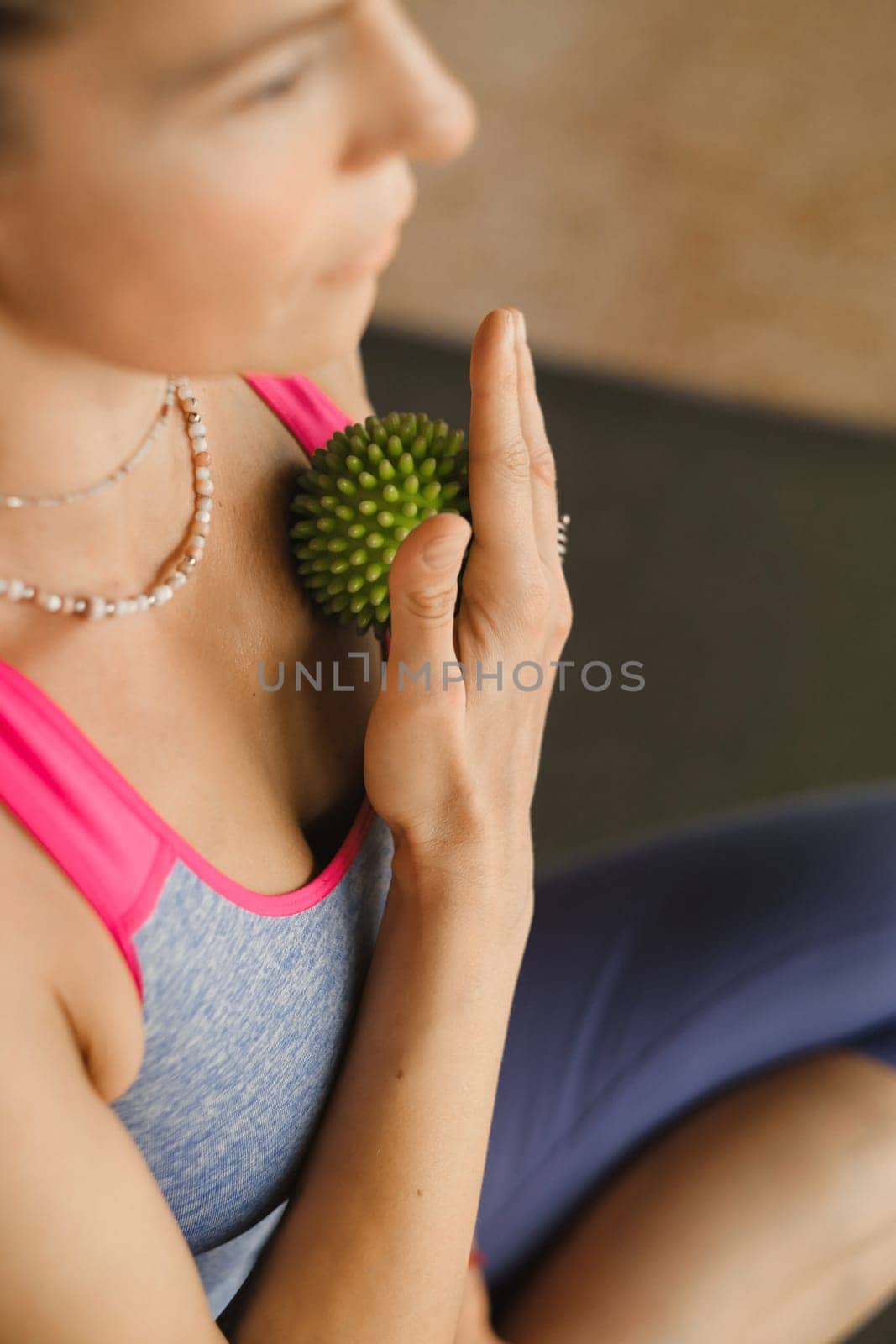 A woman does self - massage with a small ball while sitting in a fitness room . Myofascial relaxation.