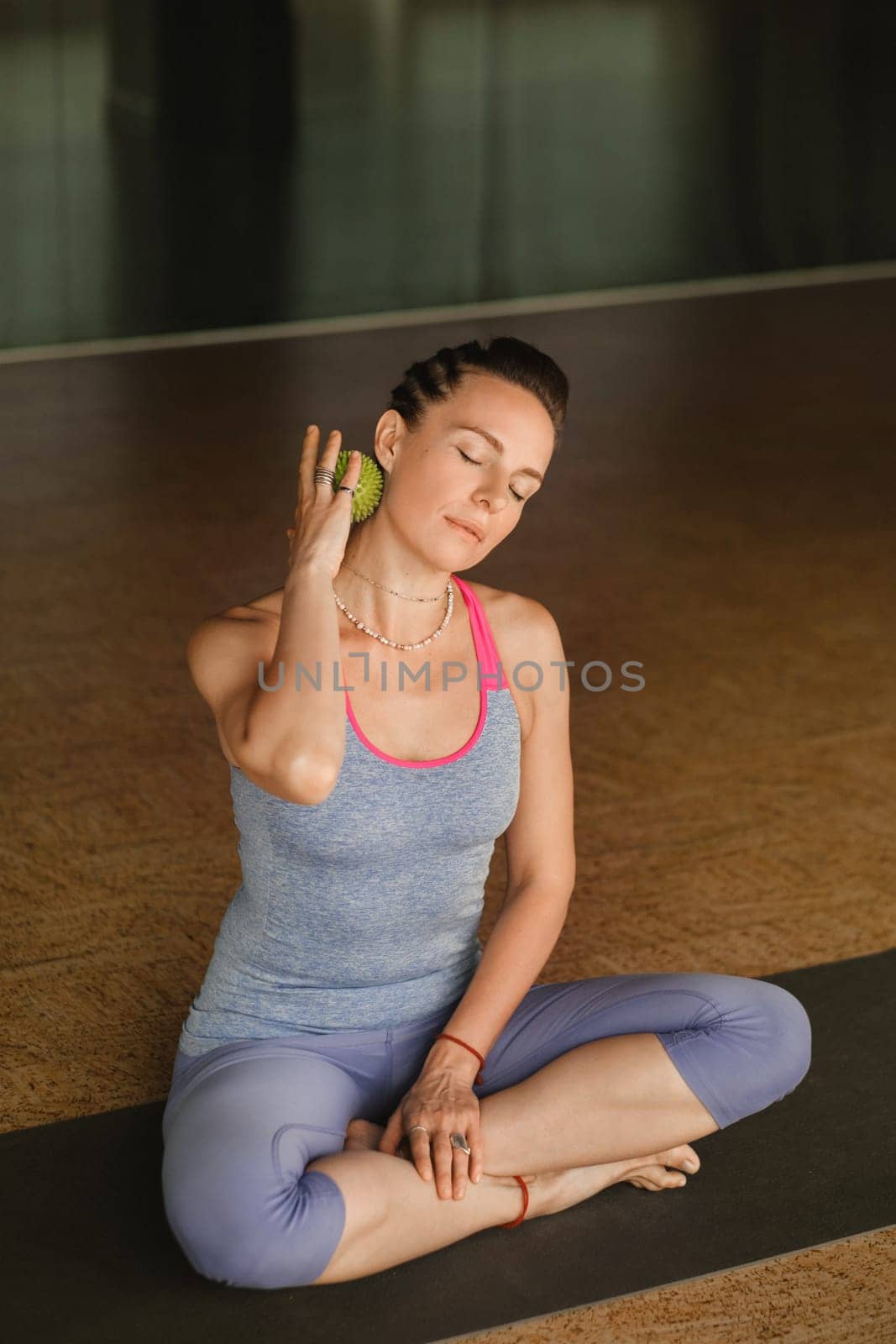 A woman does self - massage with a small ball while sitting in a fitness room . Myofascial relaxation by Lobachad