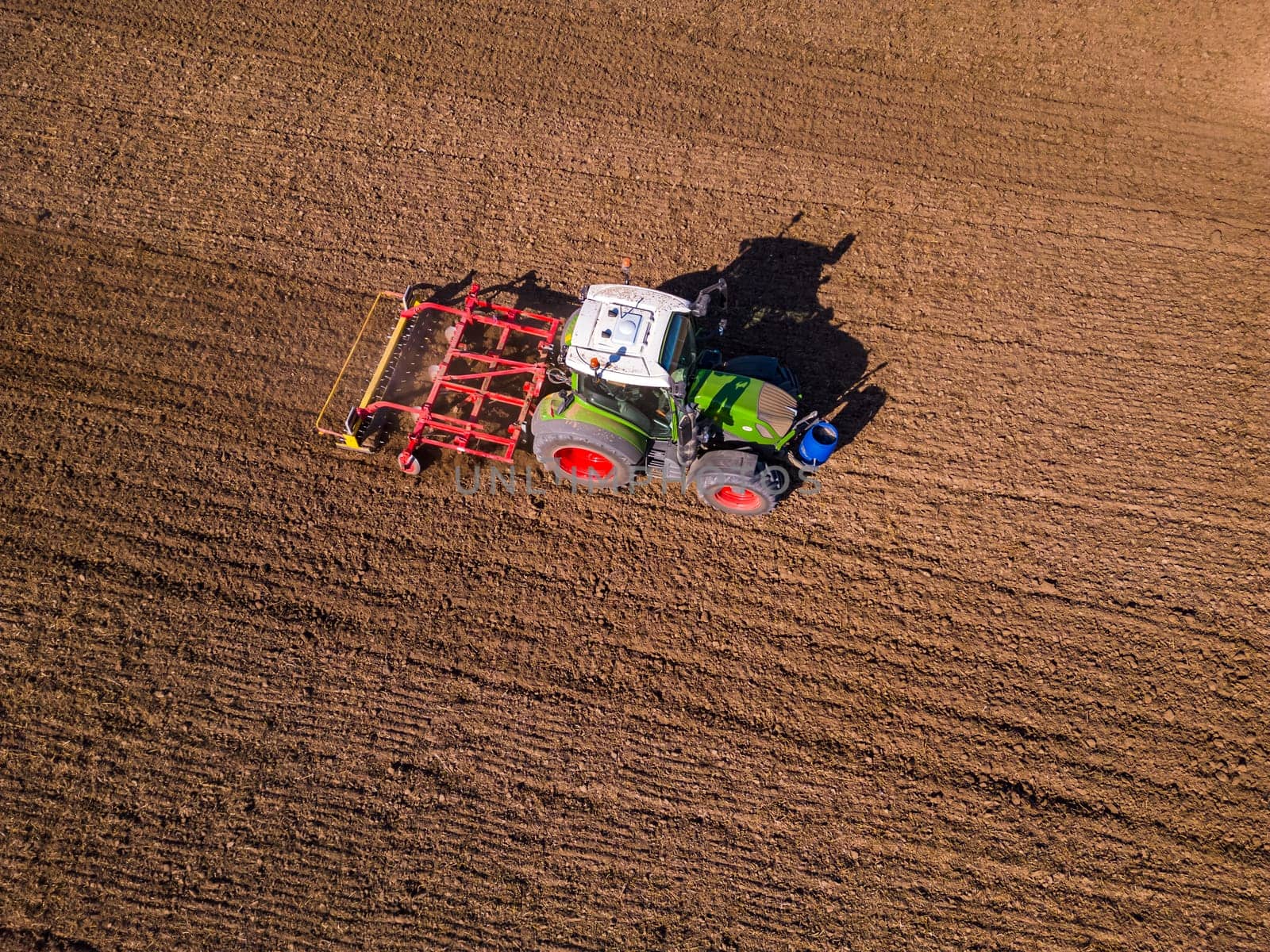 A green tractor with a red plow on a field with plowed soil seen from above as an aerial view