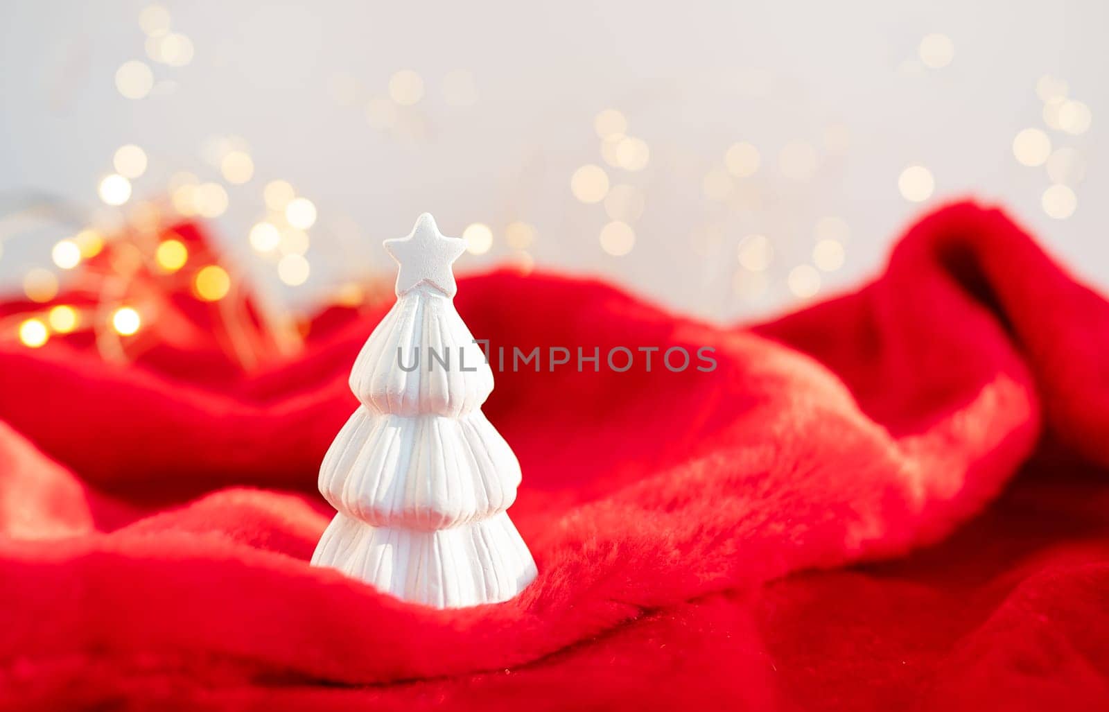 Christmas home interior with a white ceramic Christmas tree on a red plaid and bokeh with a garland in the background. Christmas and New Year concept