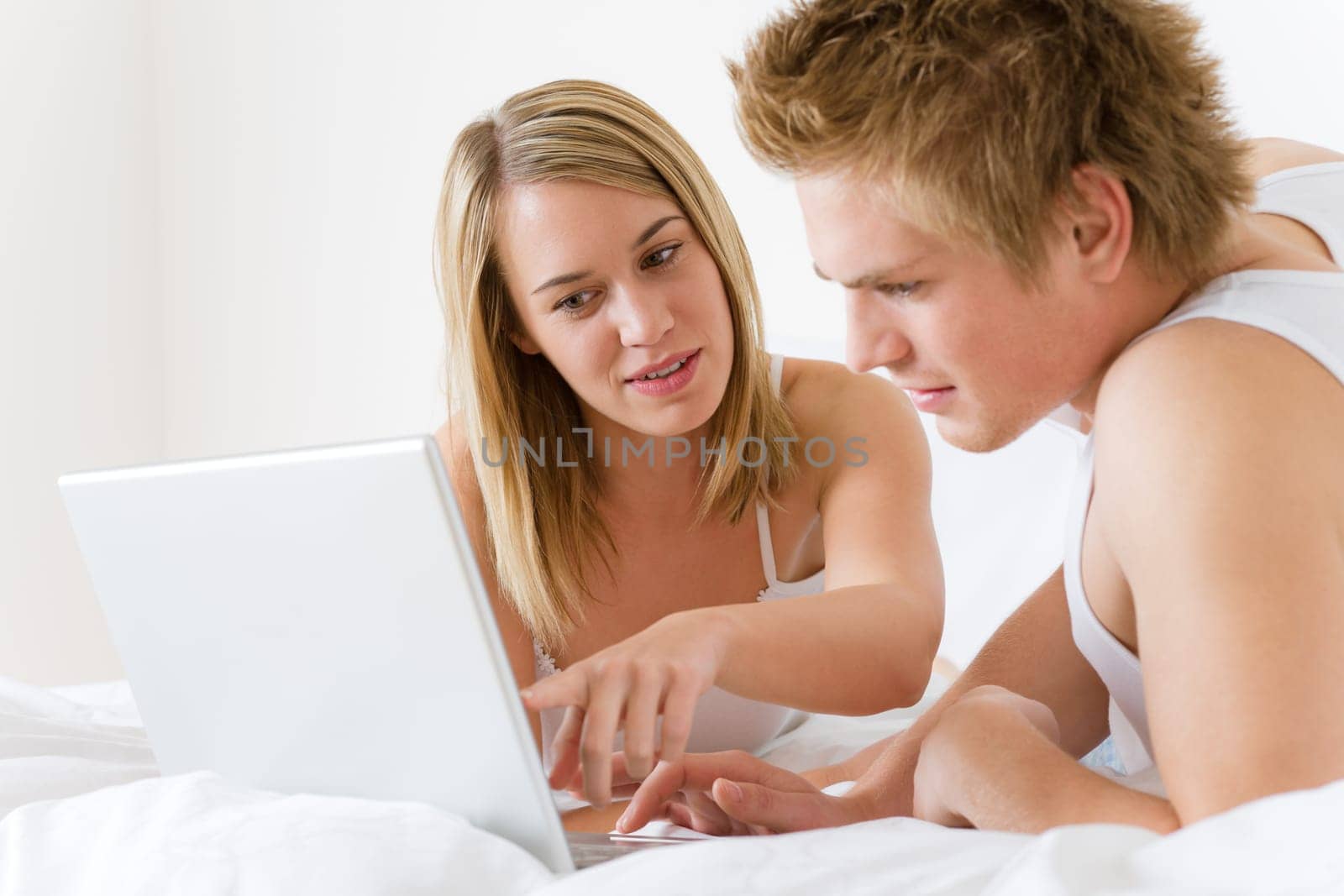 Young couple relax in bed with laptop lying down