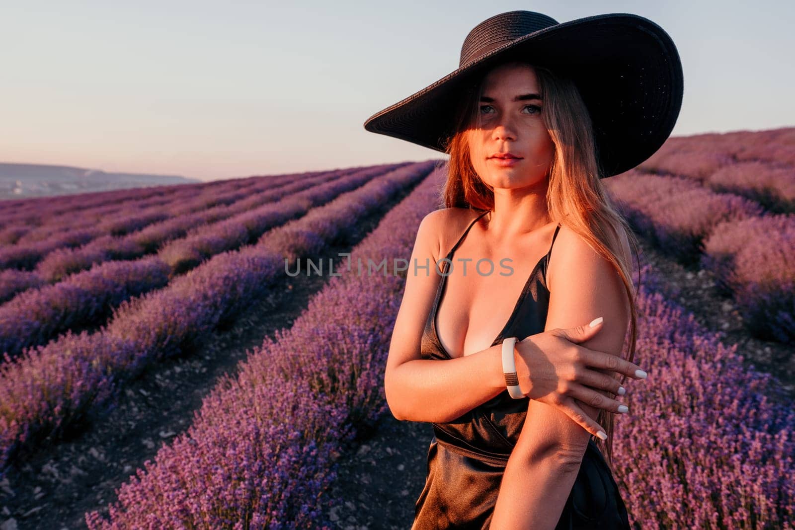 Woman lavender field. Happy carefree woman in black dress and hat with large brim walking in a lavender field during sunset. Perfect for inspirational and warm concepts in travel and wanderlust. by panophotograph