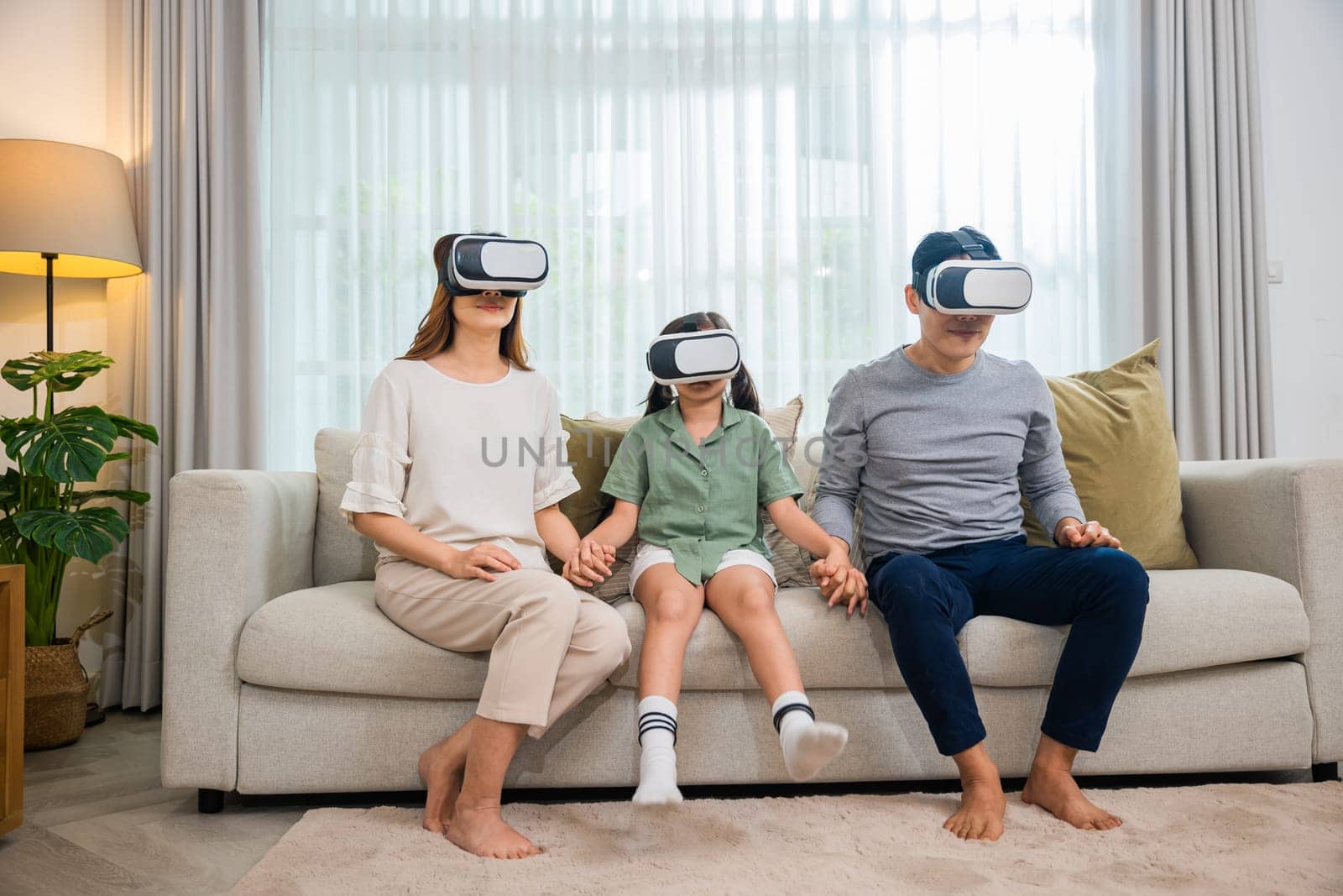 Happy family have mother father and daughter watching movie or playing video game, game entertainment innovation technology, Asian family wear vr glasses headsets excited sitting sofa in living room