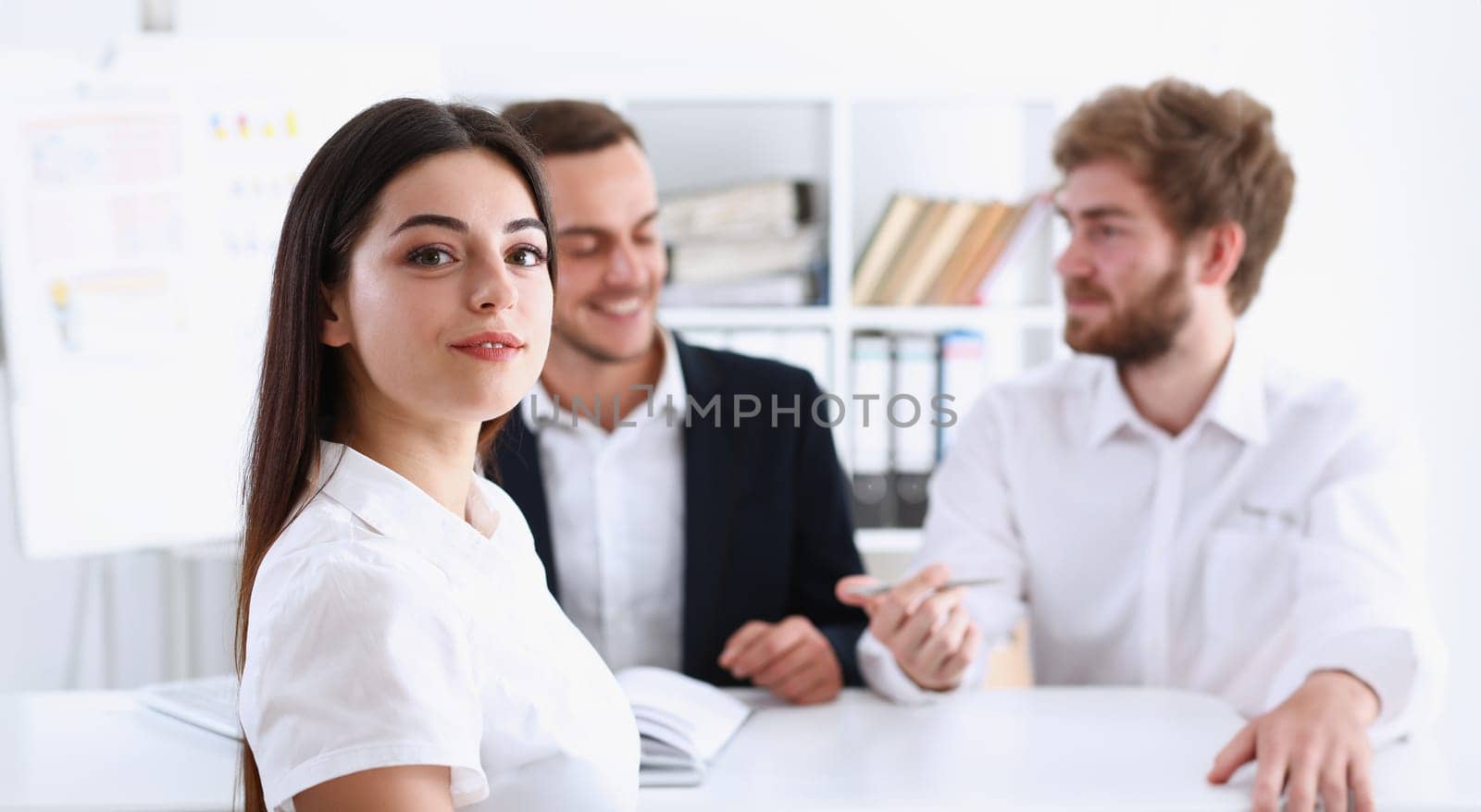 Beautiful smiling cheerful girl at workplace look in camera with colleagues group in background. White collar worker at workspace job offer modern lifestyle client visit profession train concept