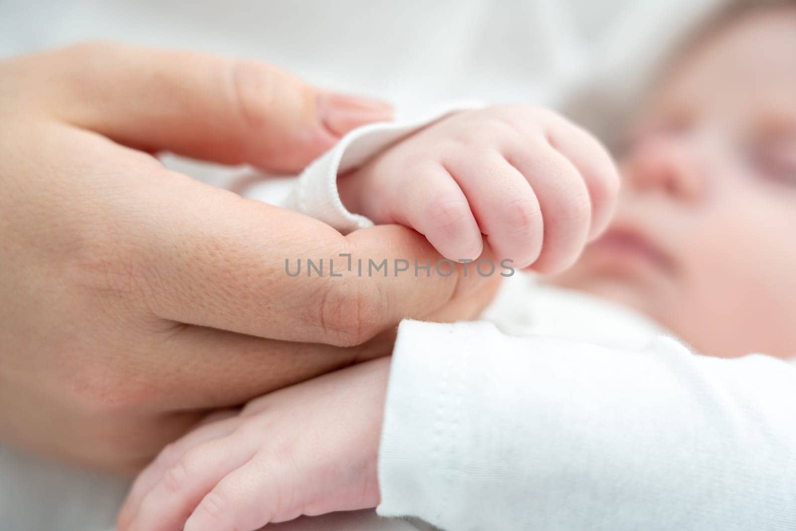 Close-up depicts a sleeping newborn's gentle hold on mother's finger, signifying pure love