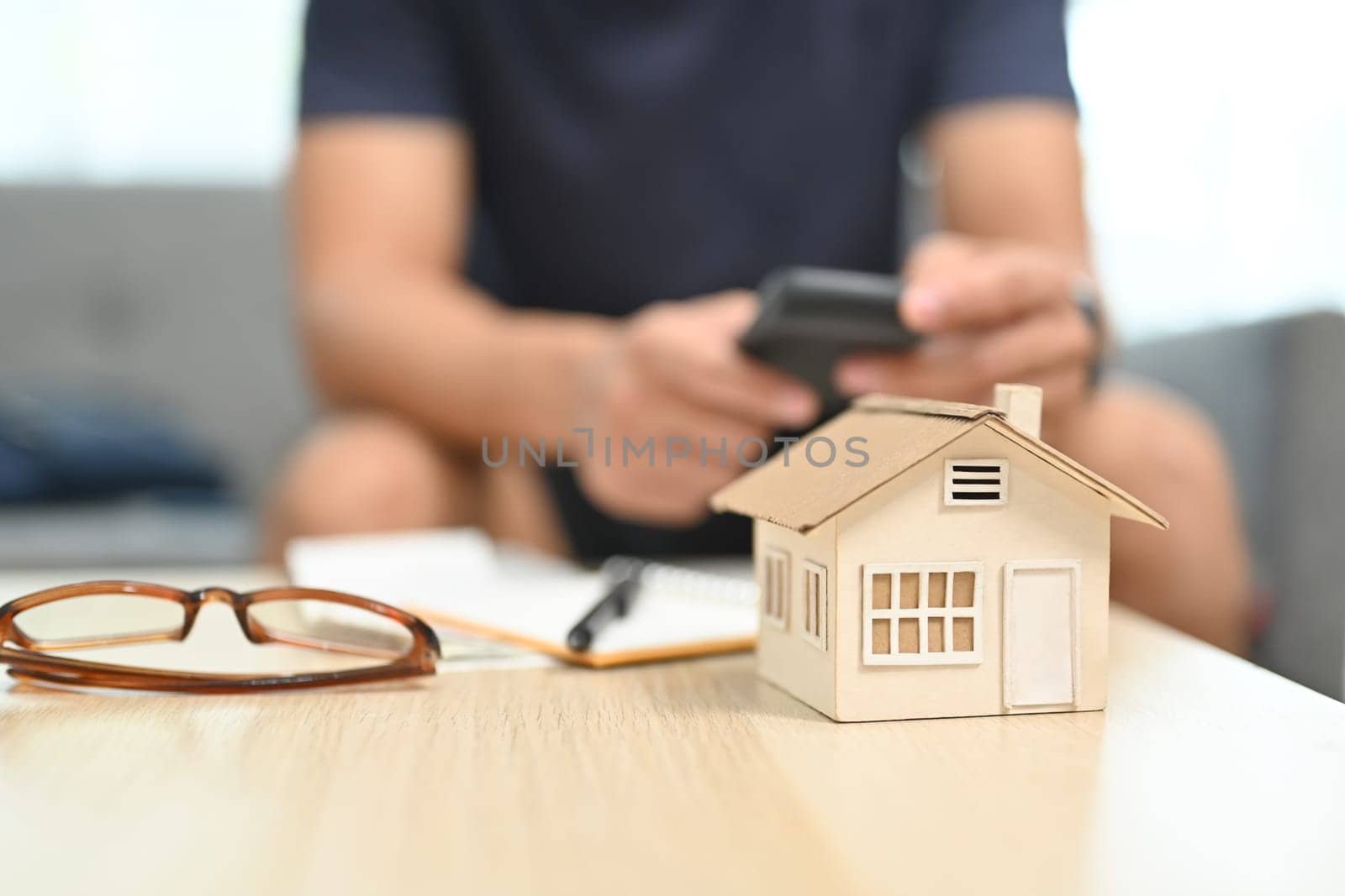 A house model, calculator and document on table with man sitting in background. Household finance concept by prathanchorruangsak