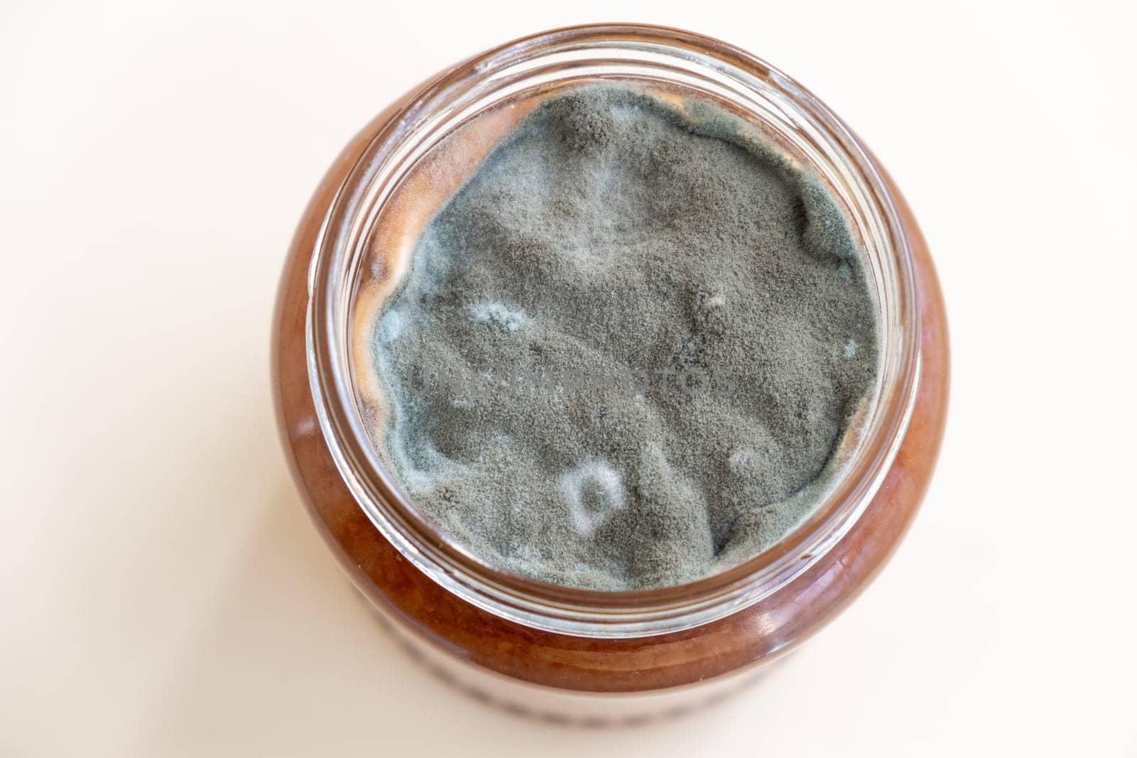 Open jar with sweet jam and mold on a white background. Mold in a jar of raspberry jam. Hazardous to health.