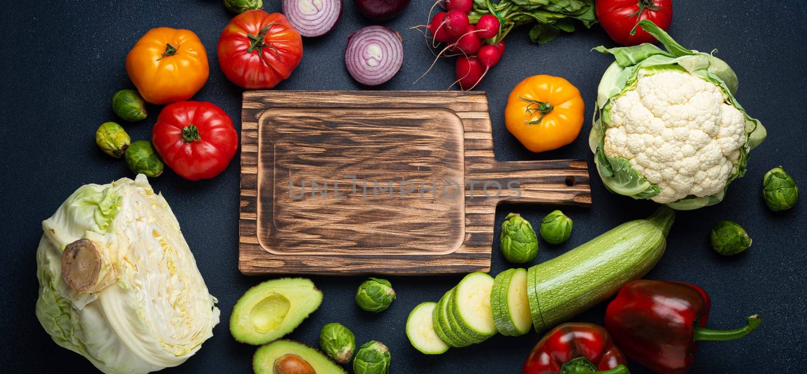 Fresh various vegetables, cut zucchini, wooden cutting board and knife on rustic dark background top view. Cooking vegetarian meal from healthy ingredients, diet food and nutrition concept