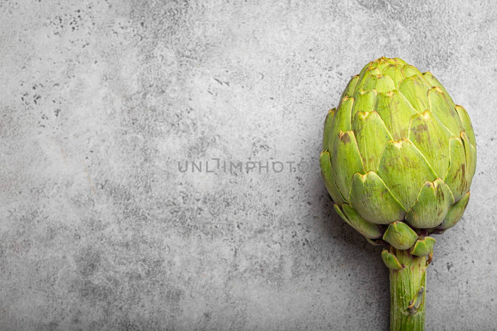 Fresh raw organic farm one artichoke on grey rustic stone background top view, healthy artichokes in balanced nutrition and cooking concept. Space for text