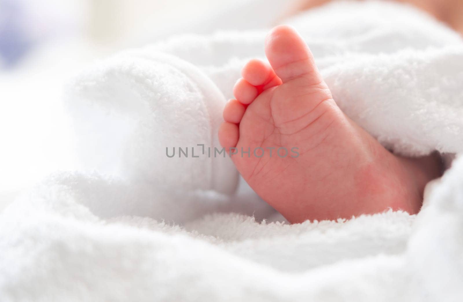 After experiencing its first bath, an infant's delicate foot playfully peeks out from a comforting soft white towel, signifying pure beginnings