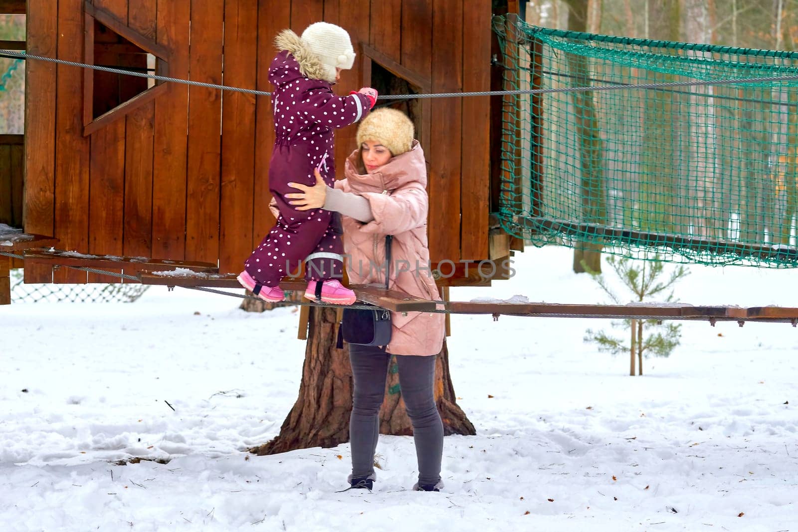 Cheerful mother with a child on a playing net stretched on trees in winter park by jovani68