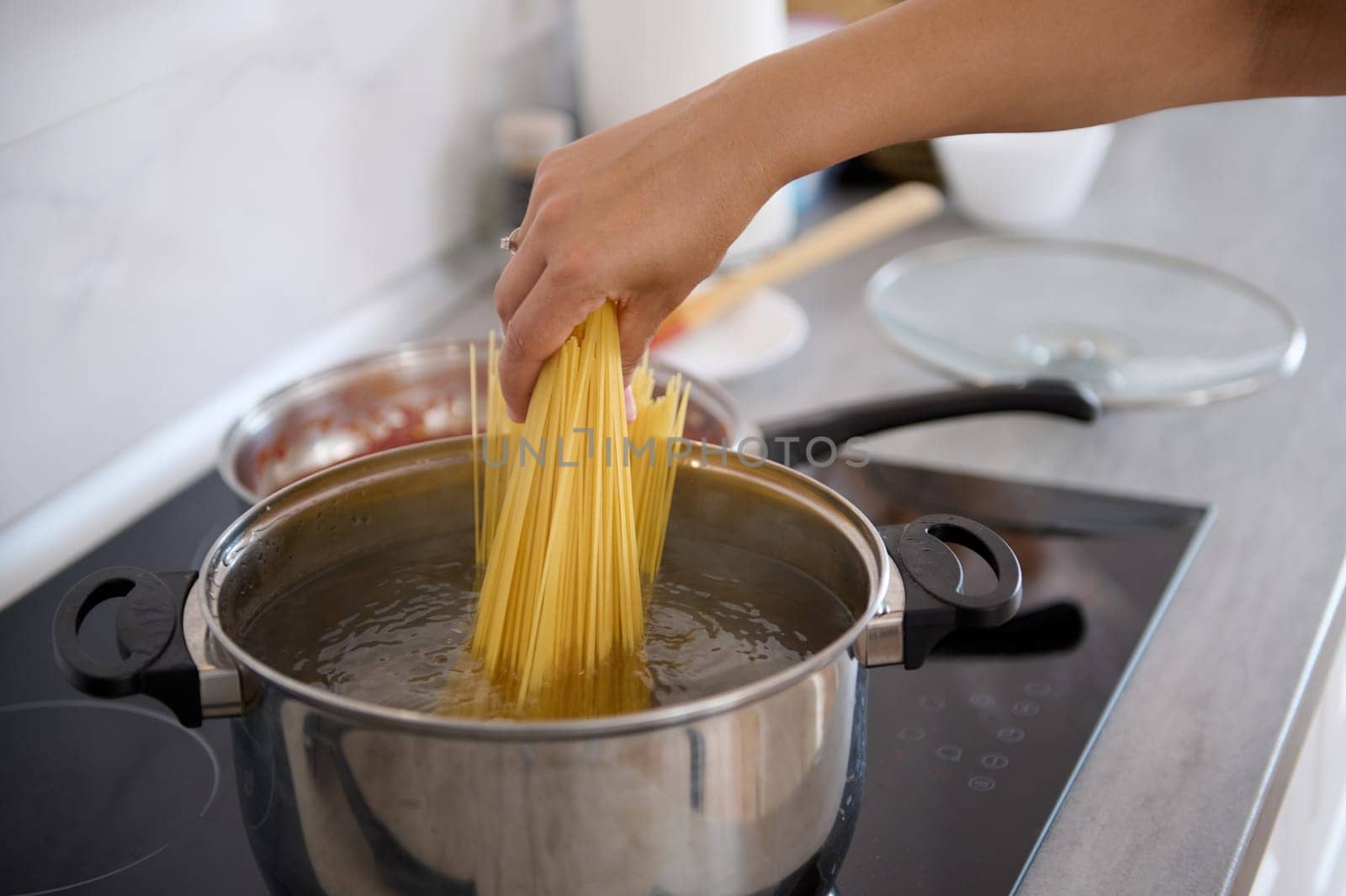 Close-up of chef hand dipping Italian pasta, wholegrain spaghetti inside a stainless steel saucepan with boiling water. Culinary. Food background