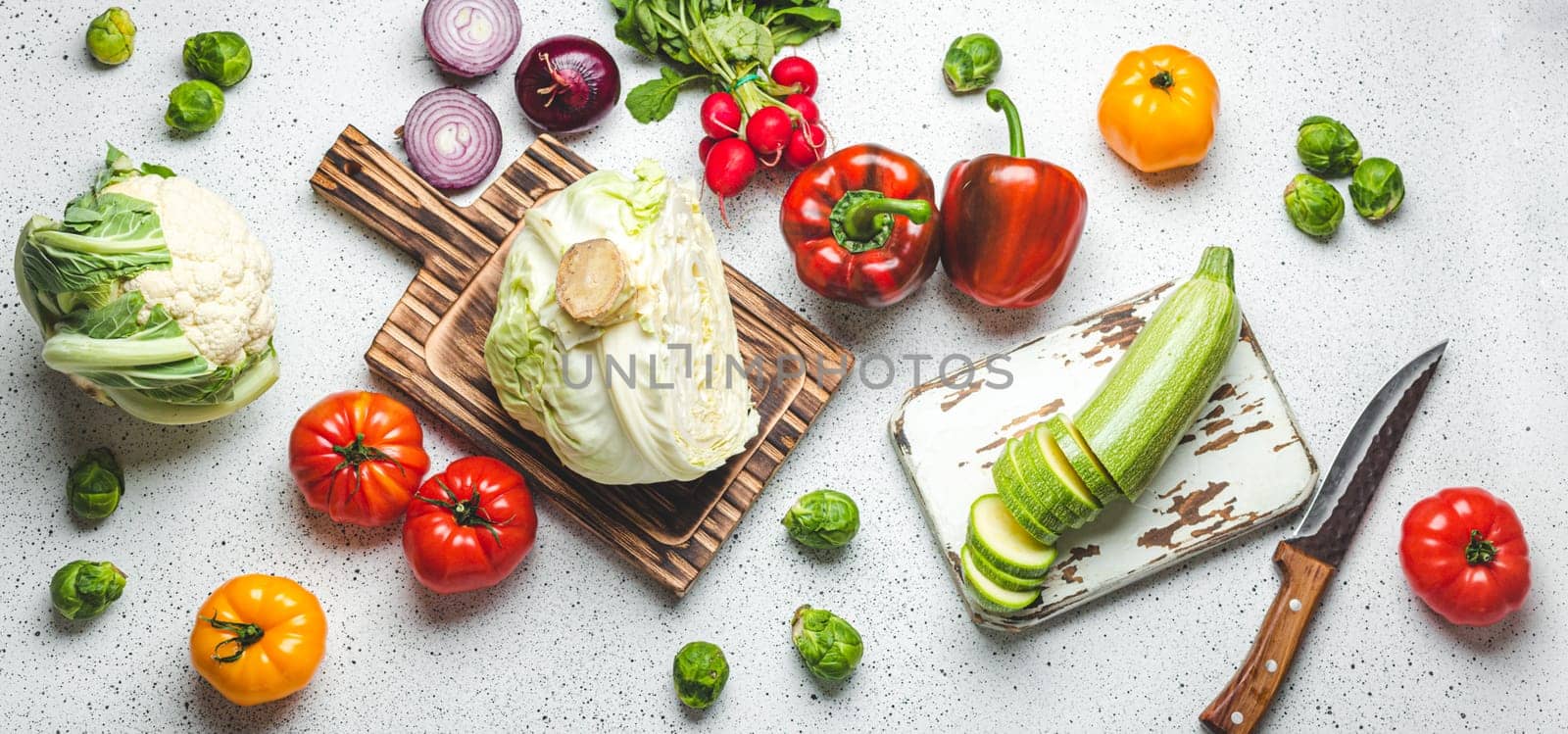 Fresh various vegetables with wooden cutting boards and knife on white kitchen table top view. Cooking vegetarian meal from healthy ingredients, diet food, nutrition concept by its_al_dente