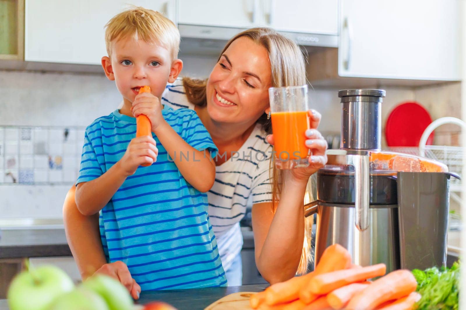 Mom and son drink fresh carrot juice squeezed using a juicer in the kitchen at home. Family nutrition, healthy eating concept