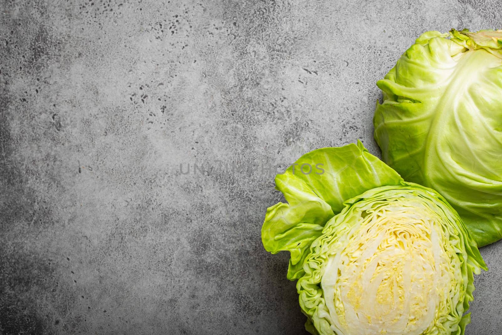 Fresh raw organic farm cabbage cut in half on grey rustic stone background top view, healthy cabbage in balanced nutrition and cooking concept. Space for text