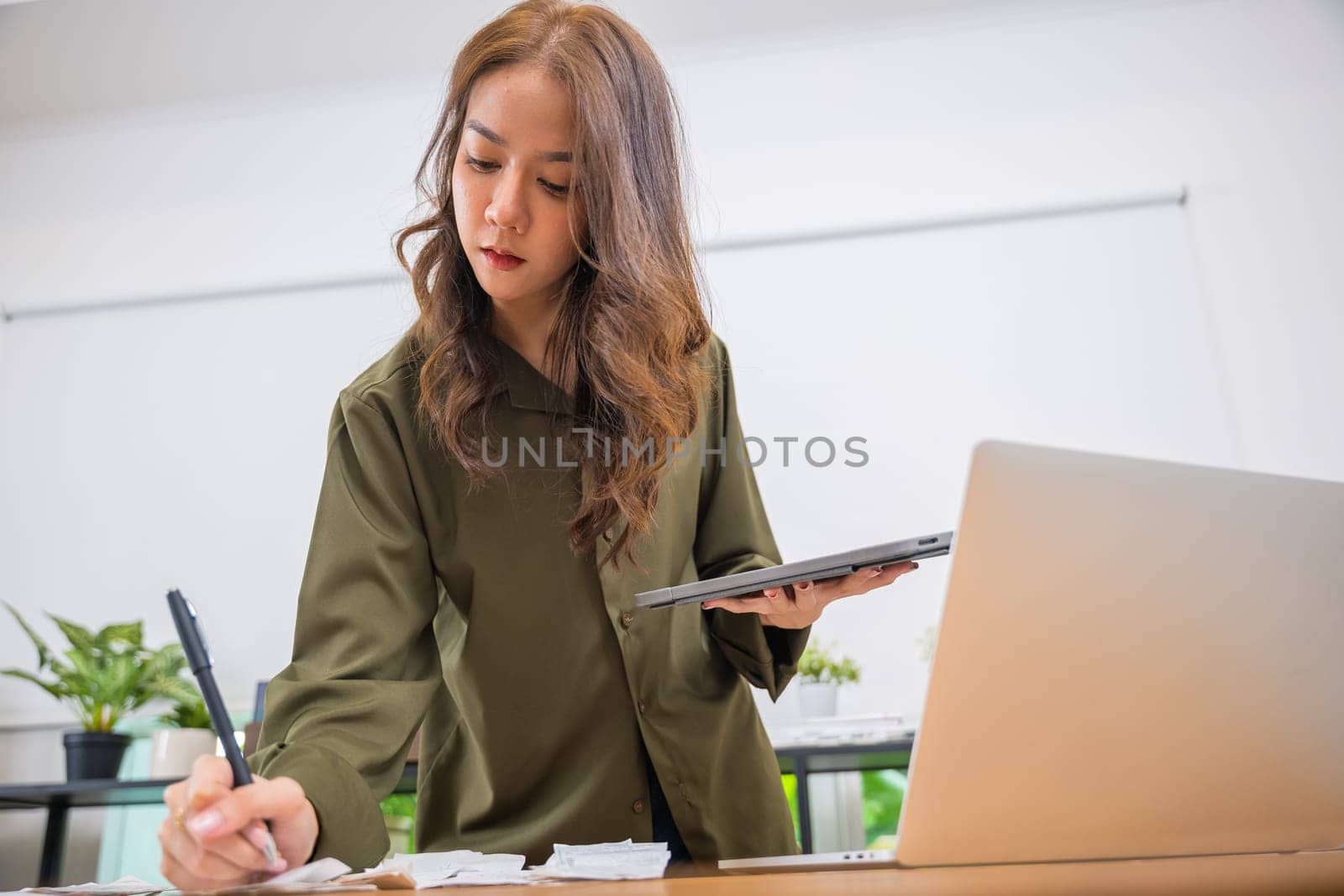 Asian female calculating family budget financial and accounting at home, young woman working with financial data calculator with tablet computer and writing make note calculate, pay bills tax online