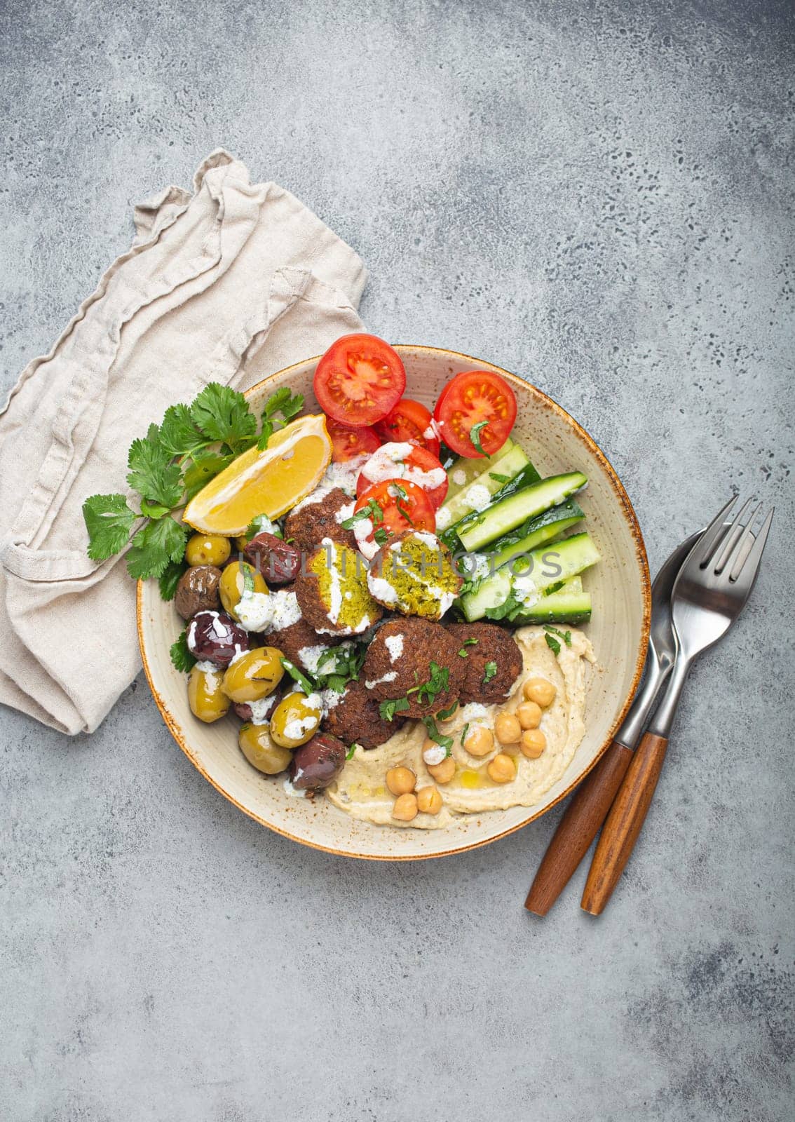 Falafel salad bowl with hummus, vegetables, olives and herbs. Vegan lunch plate top view, rustic stone background, healthy meal with falafel and veggies by its_al_dente