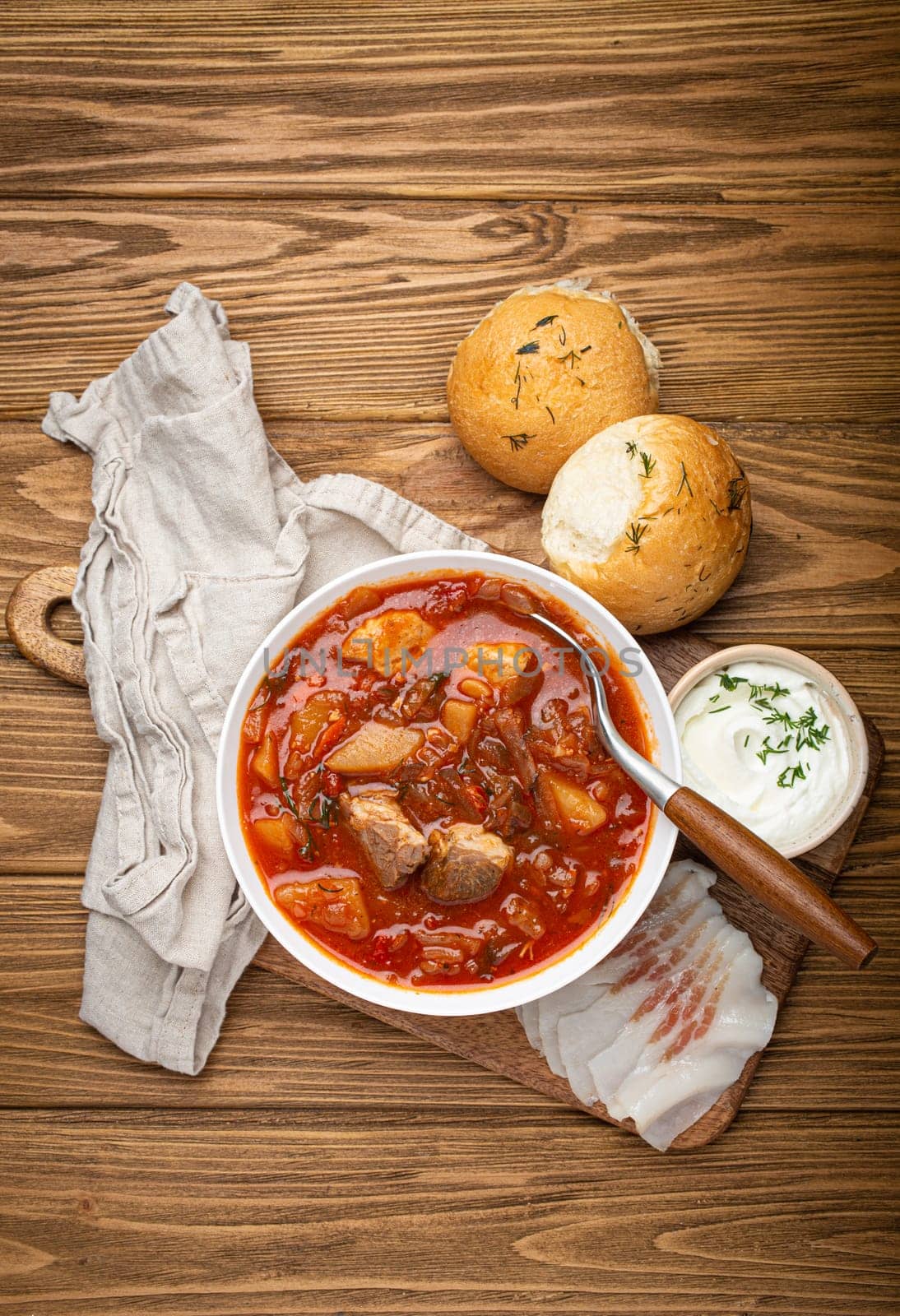 Ukrainian Borscht, red beetroot soup with meat, in white bowl with sour cream, garlic buns Pampushka and salo slices on rustic stone background. Traditional authentic dish of Ukraine