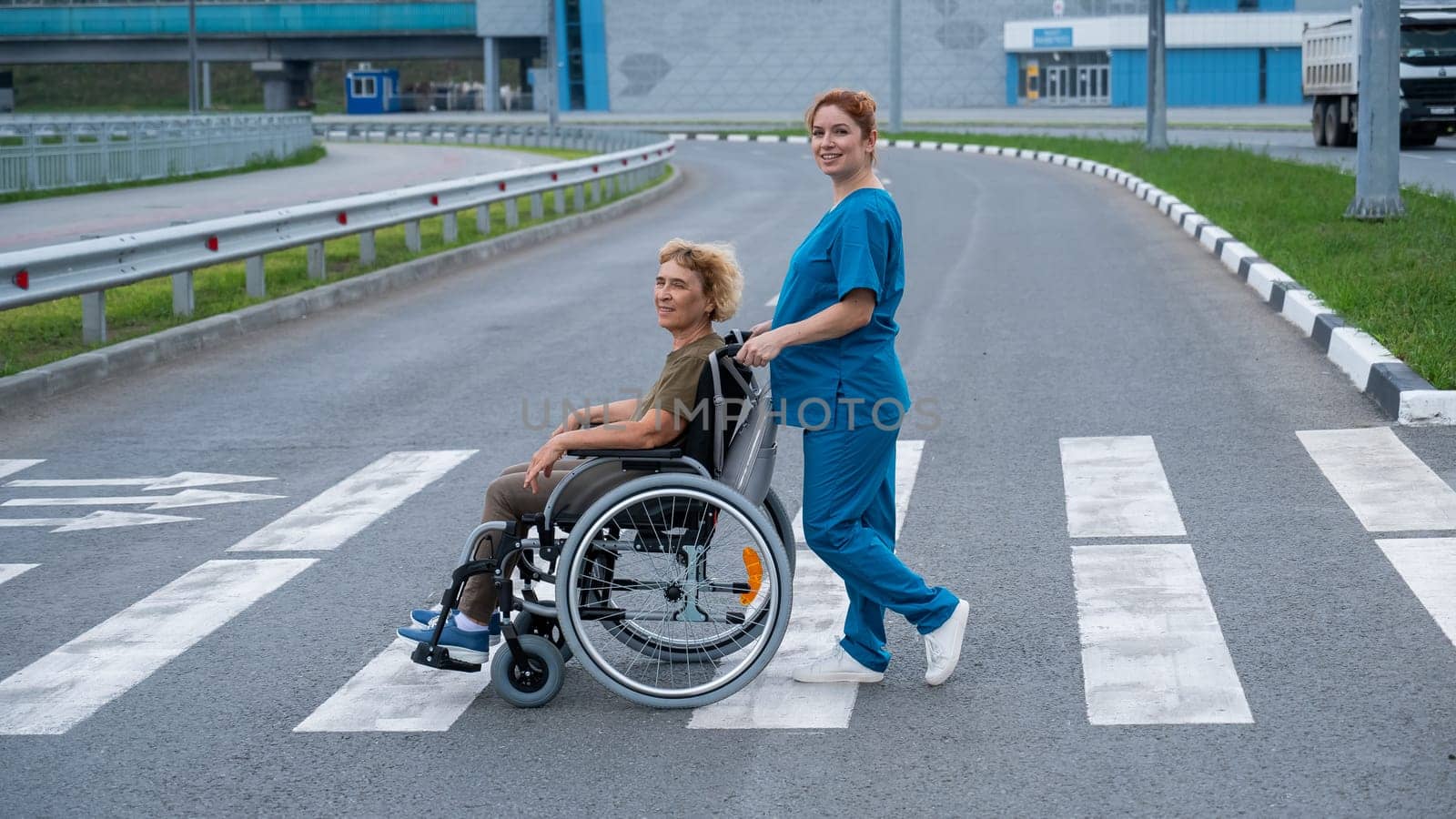 Red-haired nurse pushing an elderly woman in a wheelchair across the road. by mrwed54