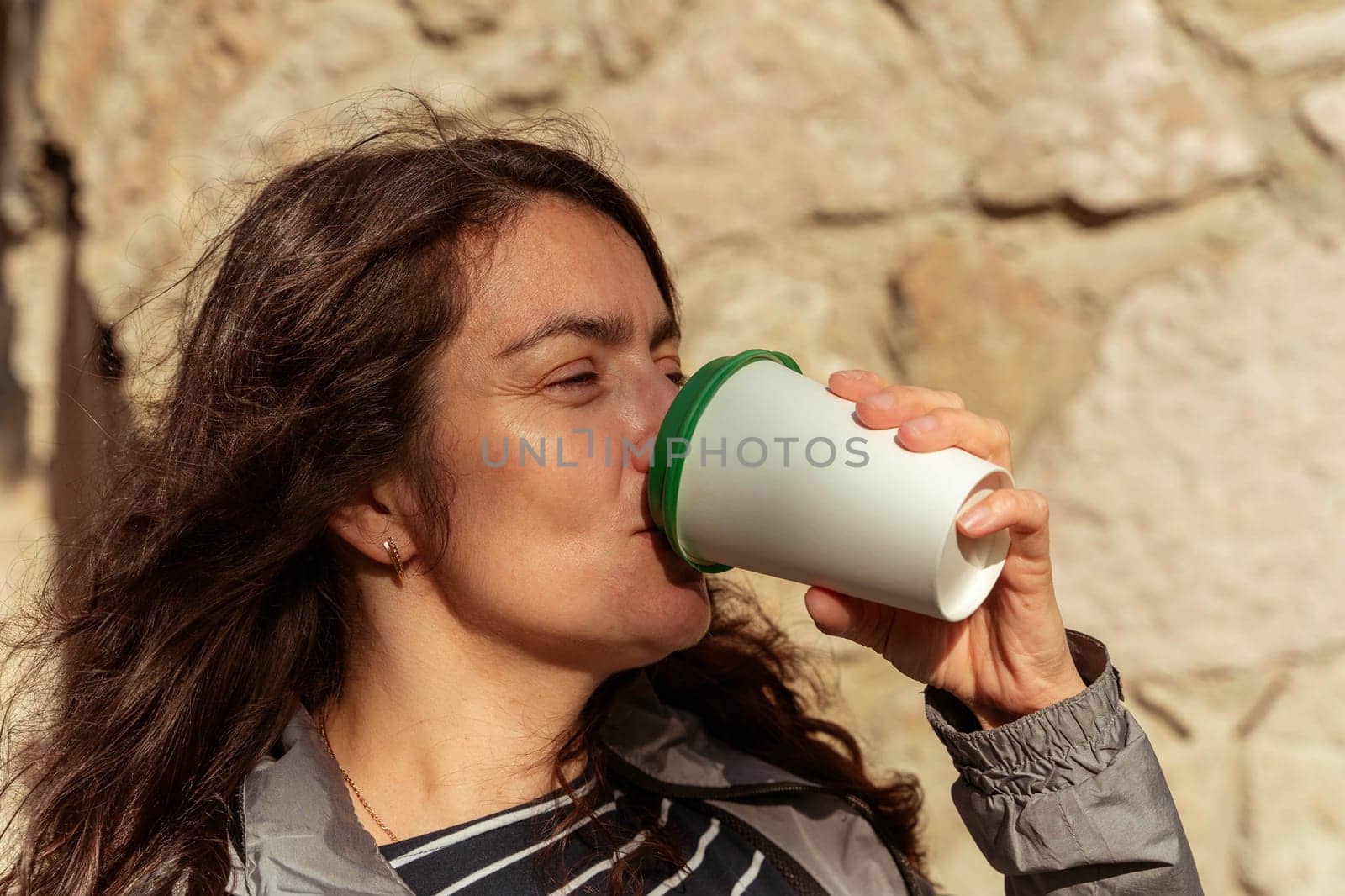 A middle-aged woman drinks coffee from a paper cup outside on a sunny autumn day by audiznam2609