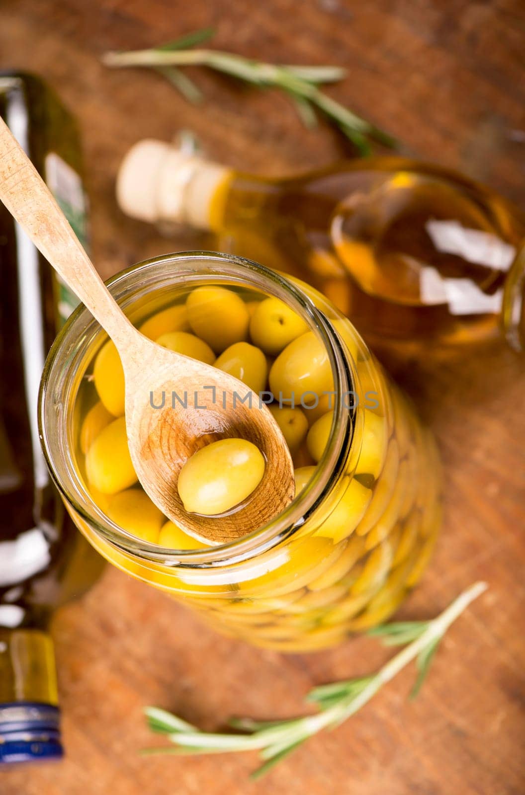 Close up green olives in wooden spoon, rosemary on a wooden background by aprilphoto