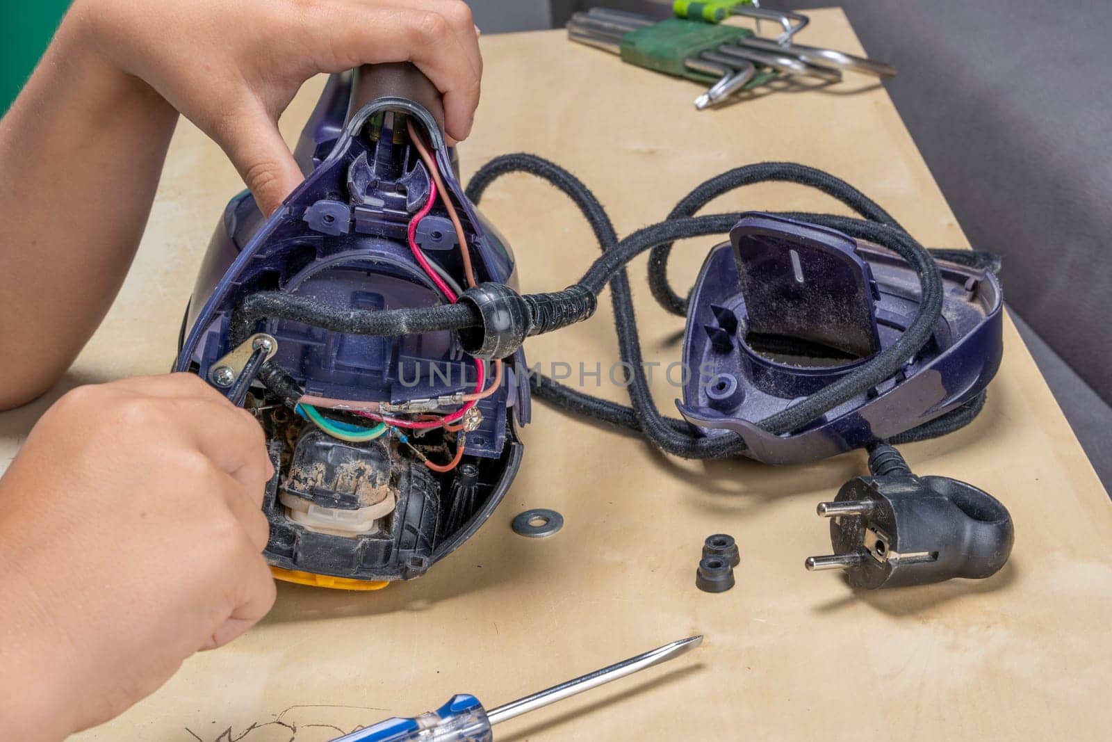 Disassembled electric iron. repairman checking and fixing broken iron. repairman checking and fixing broken steam ironusing simple tools. closeup