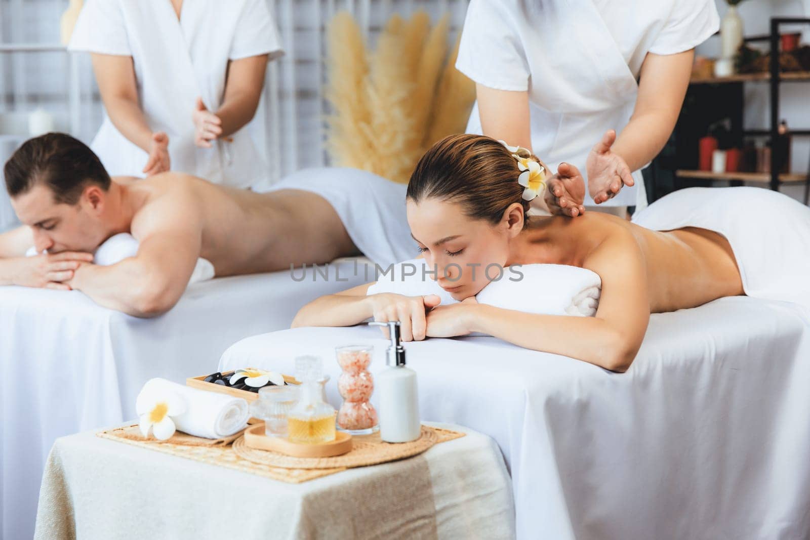 Caucasian couple customer enjoying relaxing anti-stress spa massage and pampering with beauty skin recreation leisure in day light ambient salon spa at luxury resort or hotel. Quiescent