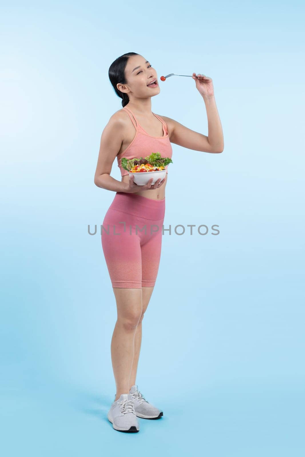 Young sporty Asian woman in sportswear holding salad bowl fill with vibrant of fruit and vegetable. Natural youthful and fit body lifestyle with balance nutrition on isolated background. Vigorous