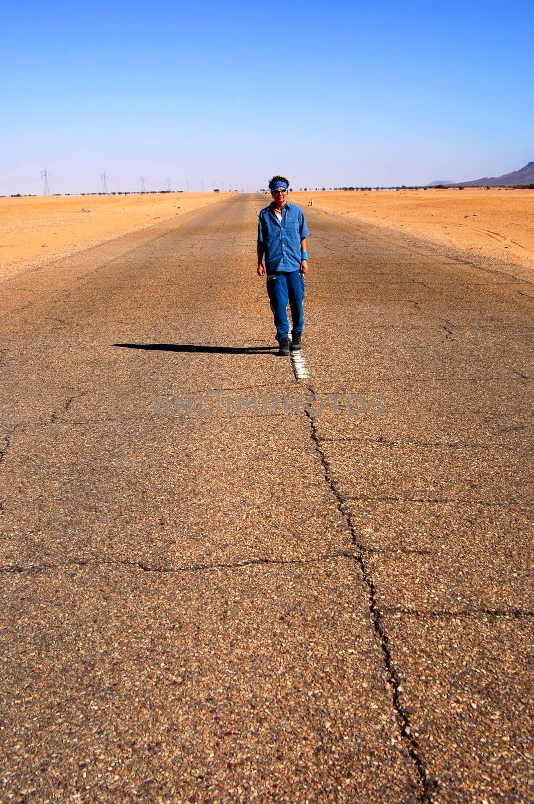 Woman running in the middle of a long straight country road near Al Awaynat,Libya