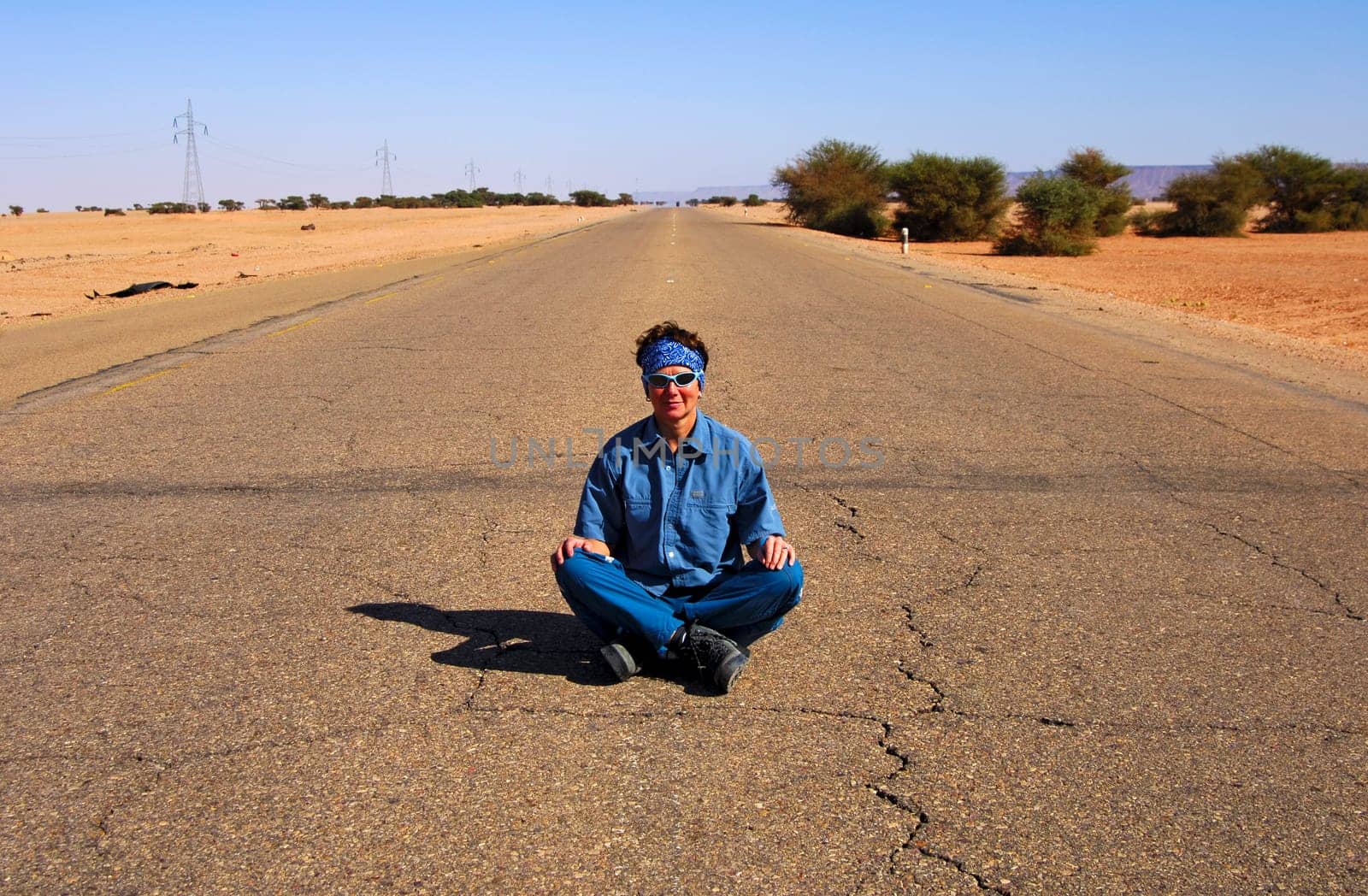 Young woman sitting cross-legged in the middle on the asphalt strip of a country road