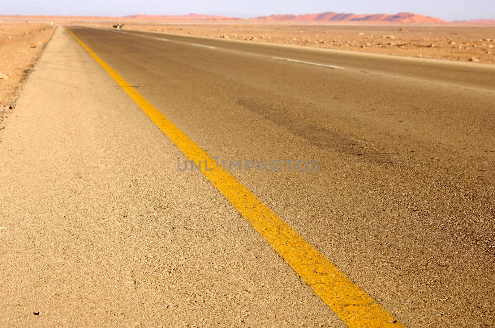Tarred road with diagonal yellow boundary line at the edge of the Sahara near Al Aw