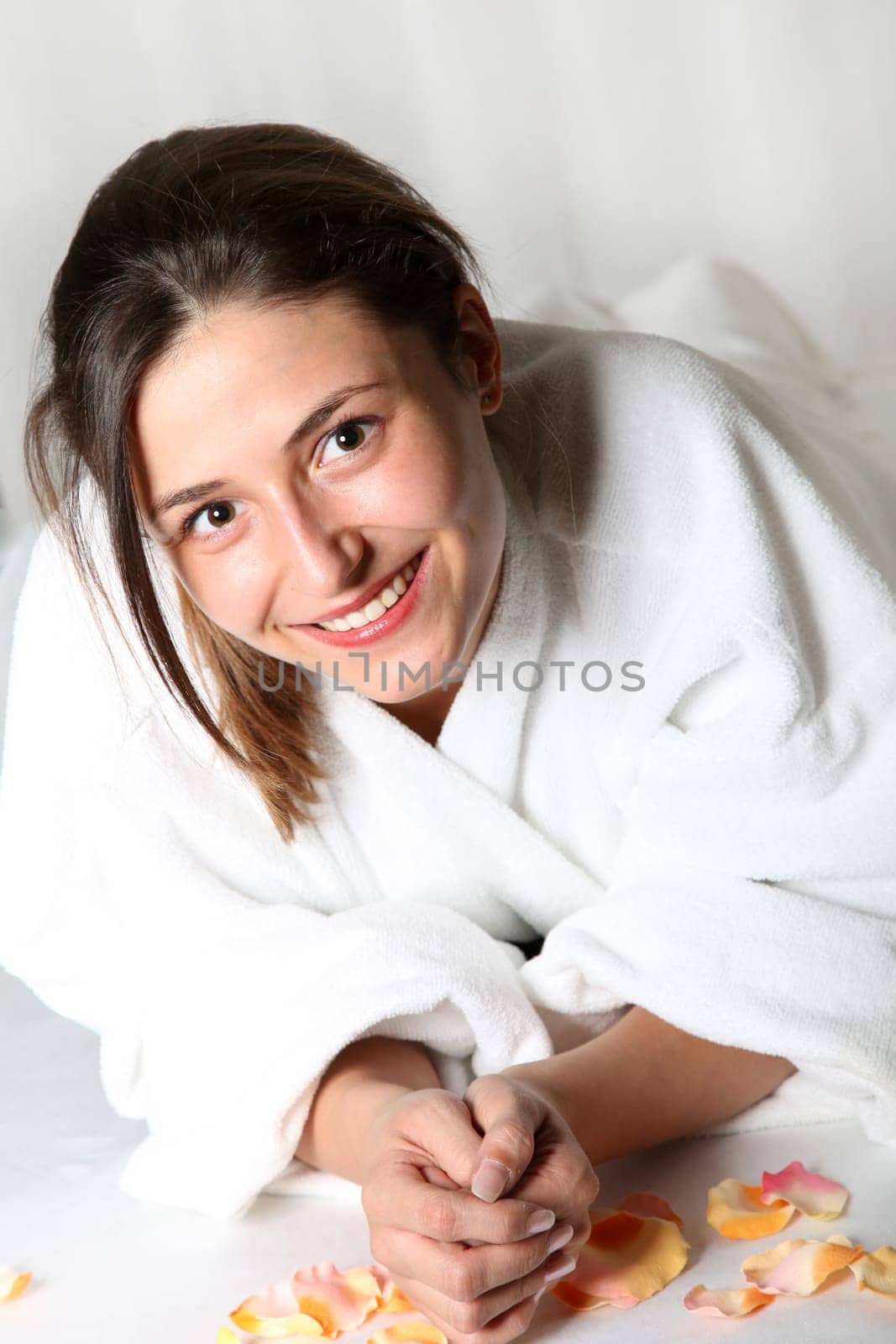 Smiling woman in bathrobe lying on rose petals