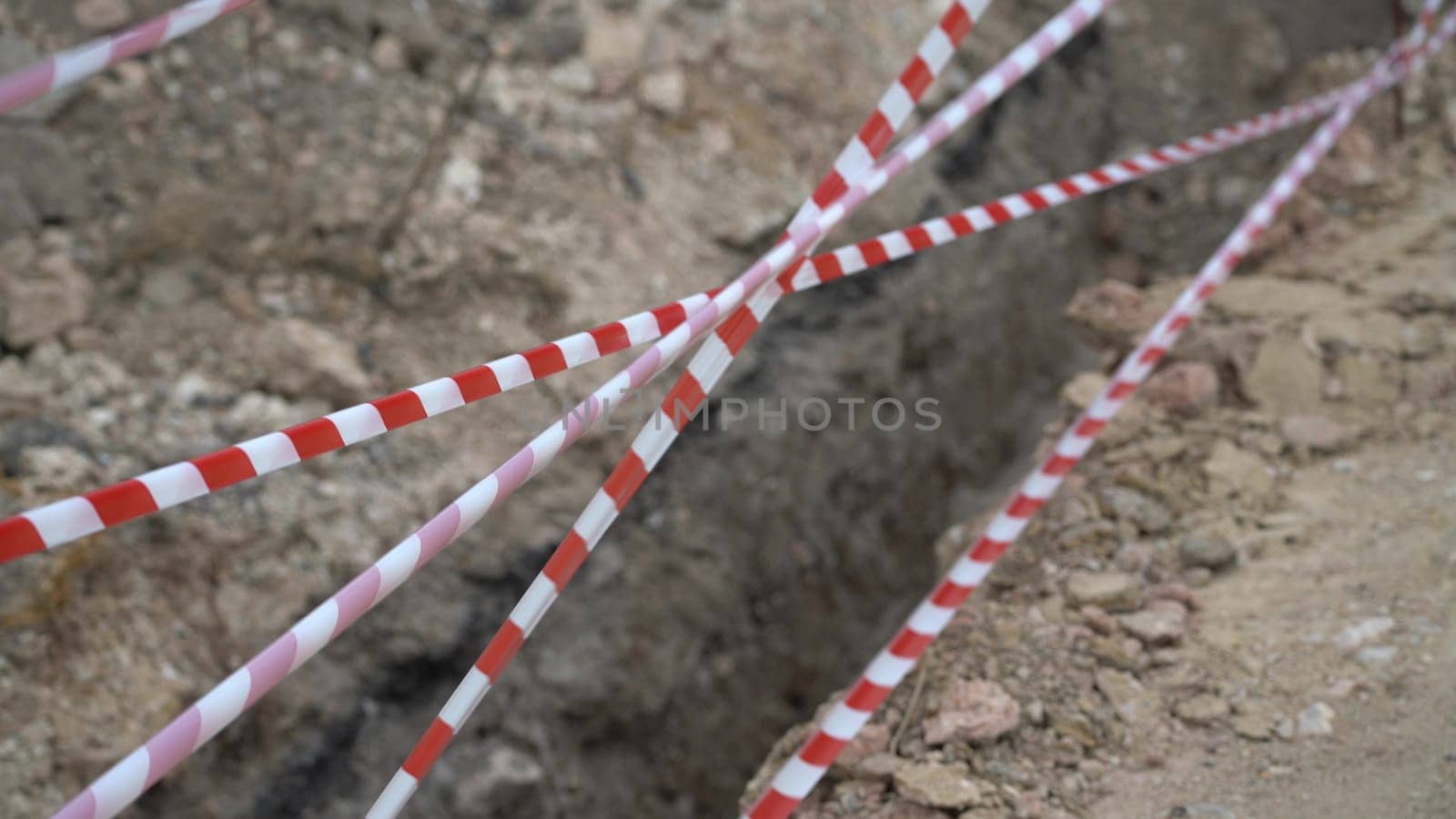 Red white barrier tape trenches. Focus on red and white barrier tape at construction site. Ribbons indicate dug trenches