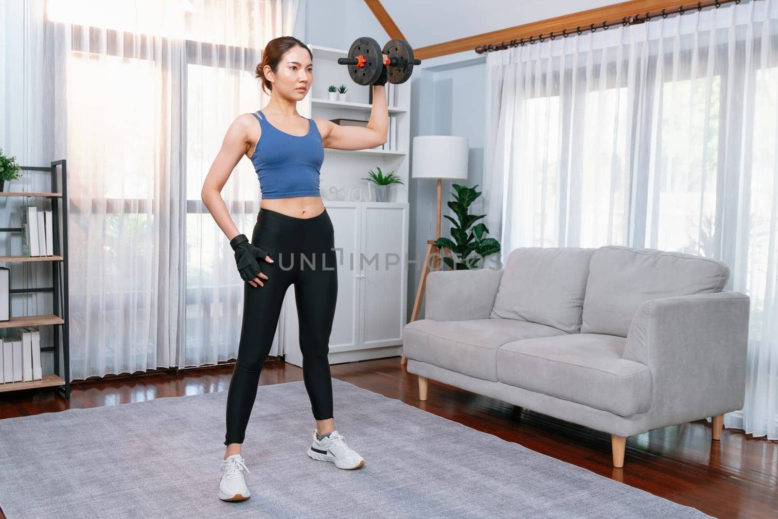 Vigorous energetic woman doing dumbbell weight lifting exercise at home. Young athletic asian woman strength and endurance training session as home workout routine.