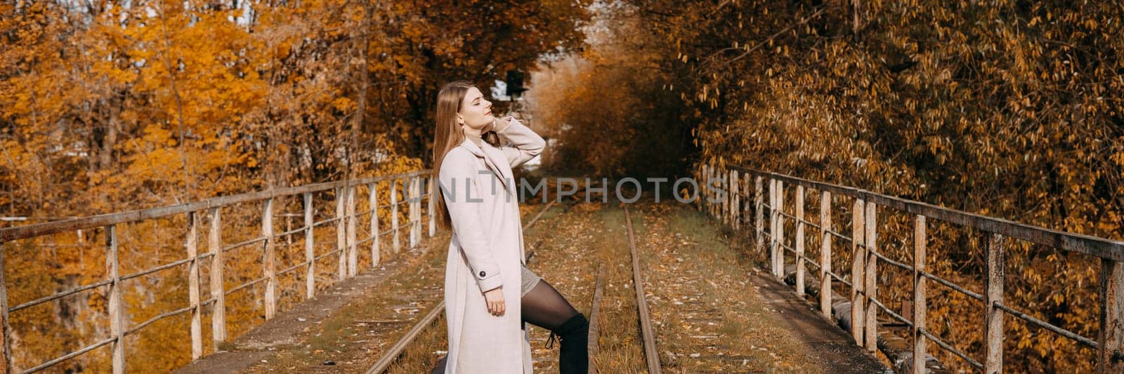 A beautiful long-haired woman walks through the autumn streets. Railway, autumn leaves, a woman in a light coat.