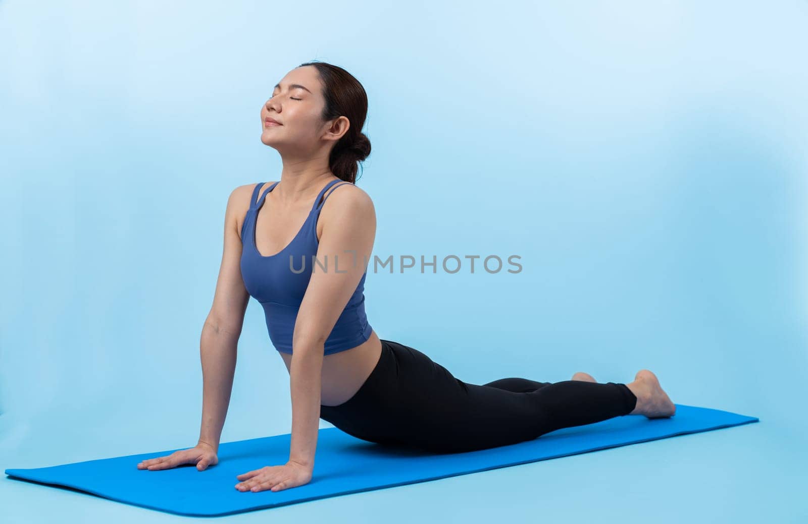 Asian woman in sportswear doing yoga exercise on fitness mat as her workout training routine. Healthy body care and calm meditation in yoga lifestyle in full body shot on isolated background. Vigorous