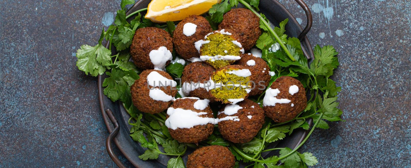 Plate of fried falafel balls served with fresh green cilantro and lemon top view on rustic concrete background. Traditional vegan dish of Middle Eastern cuisine