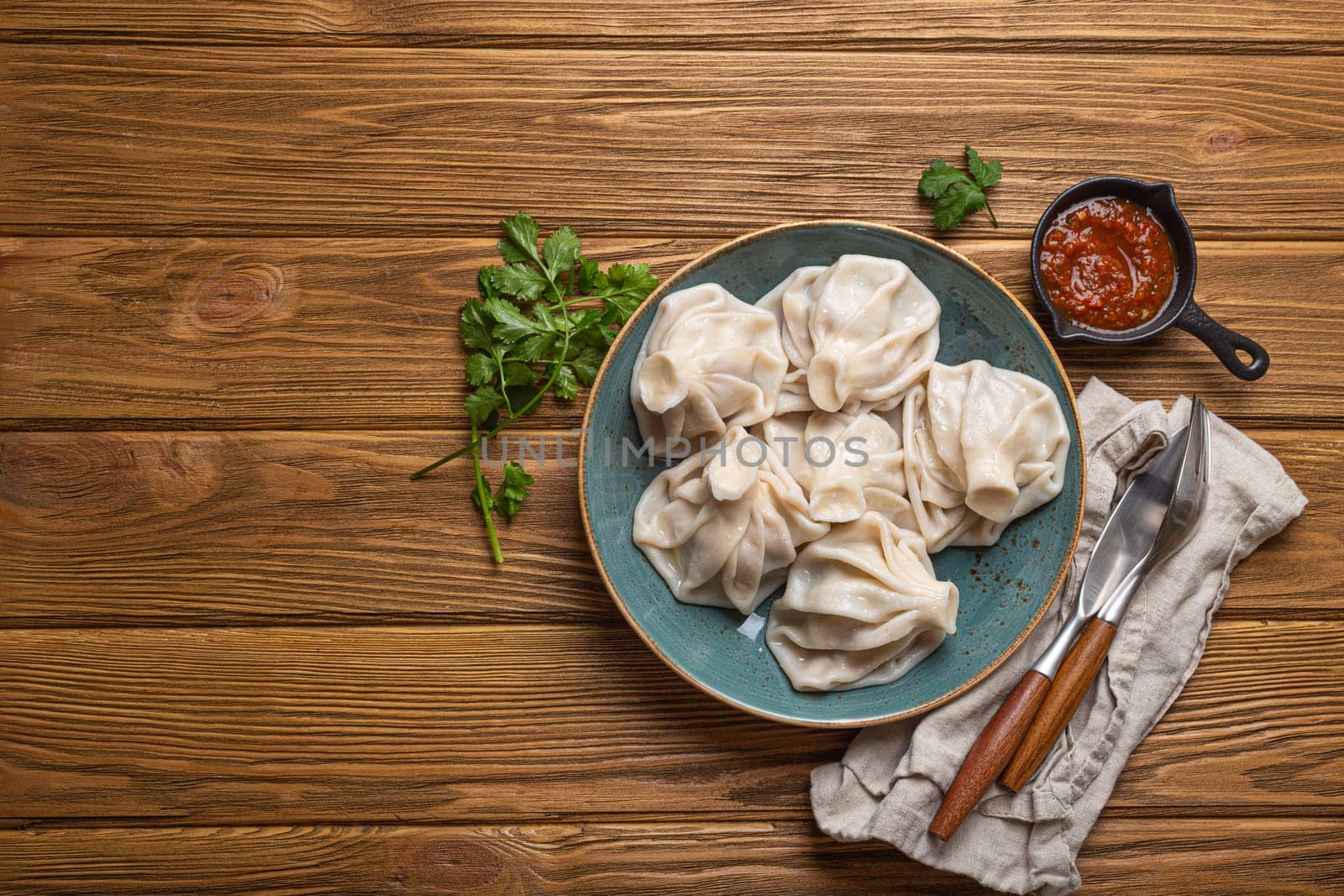Georgian dumplings Khinkali on plate with red tomato sauce and fresh cilantro top view on rustic wooden background, traditional dish of Georgia, space for text