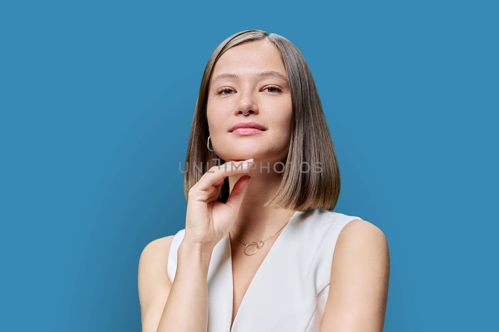 Beauty portrait of young attractive fashionable woman with natural trendy makeup, lips eyelashes eyebrows, hairstyle on blue studio background. Healthy hair, healthy skin, care, cosmetics concept